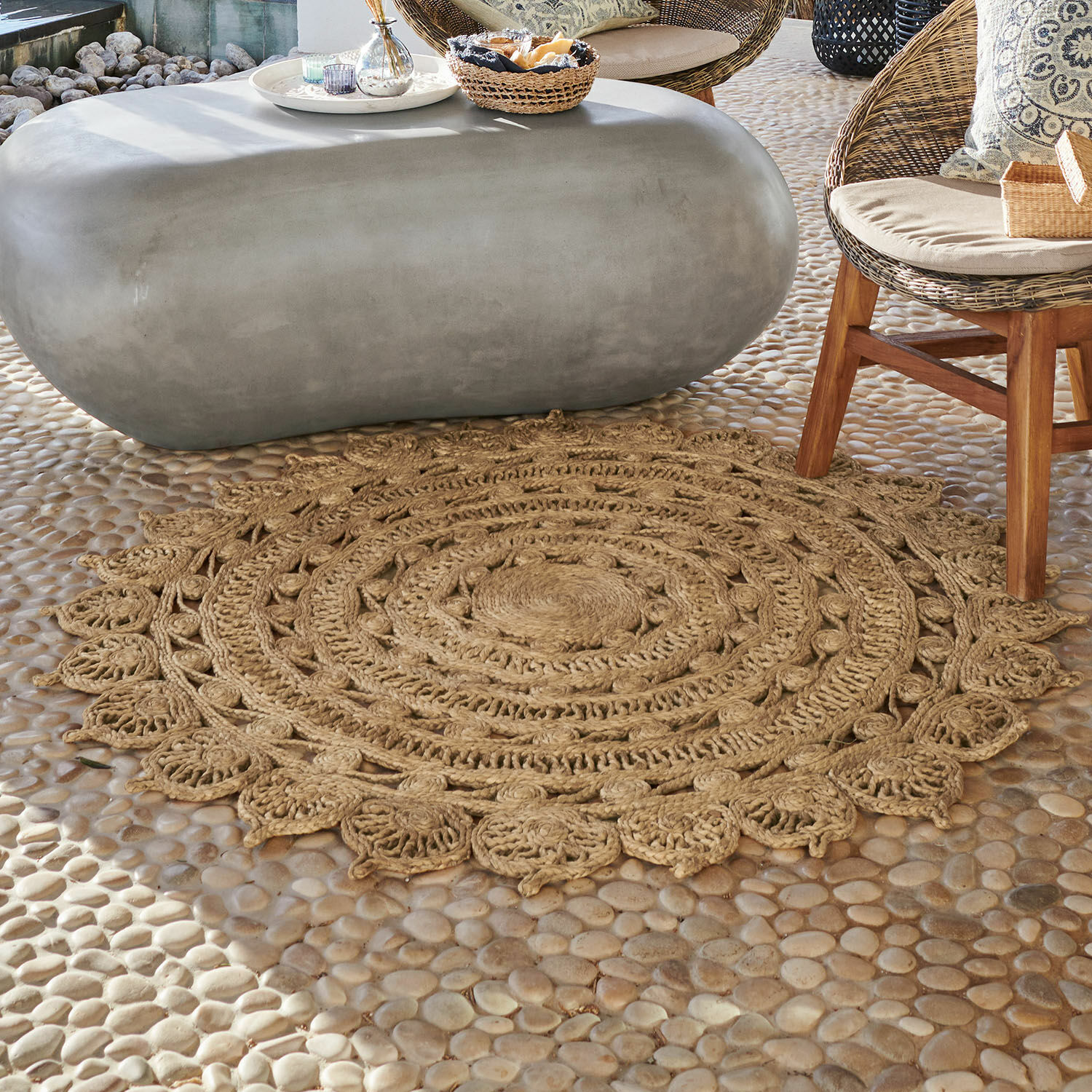 Ronde jute vloerkleed in natuurlijke kleur op stenen vloer bij rotan meubels in woonkamer