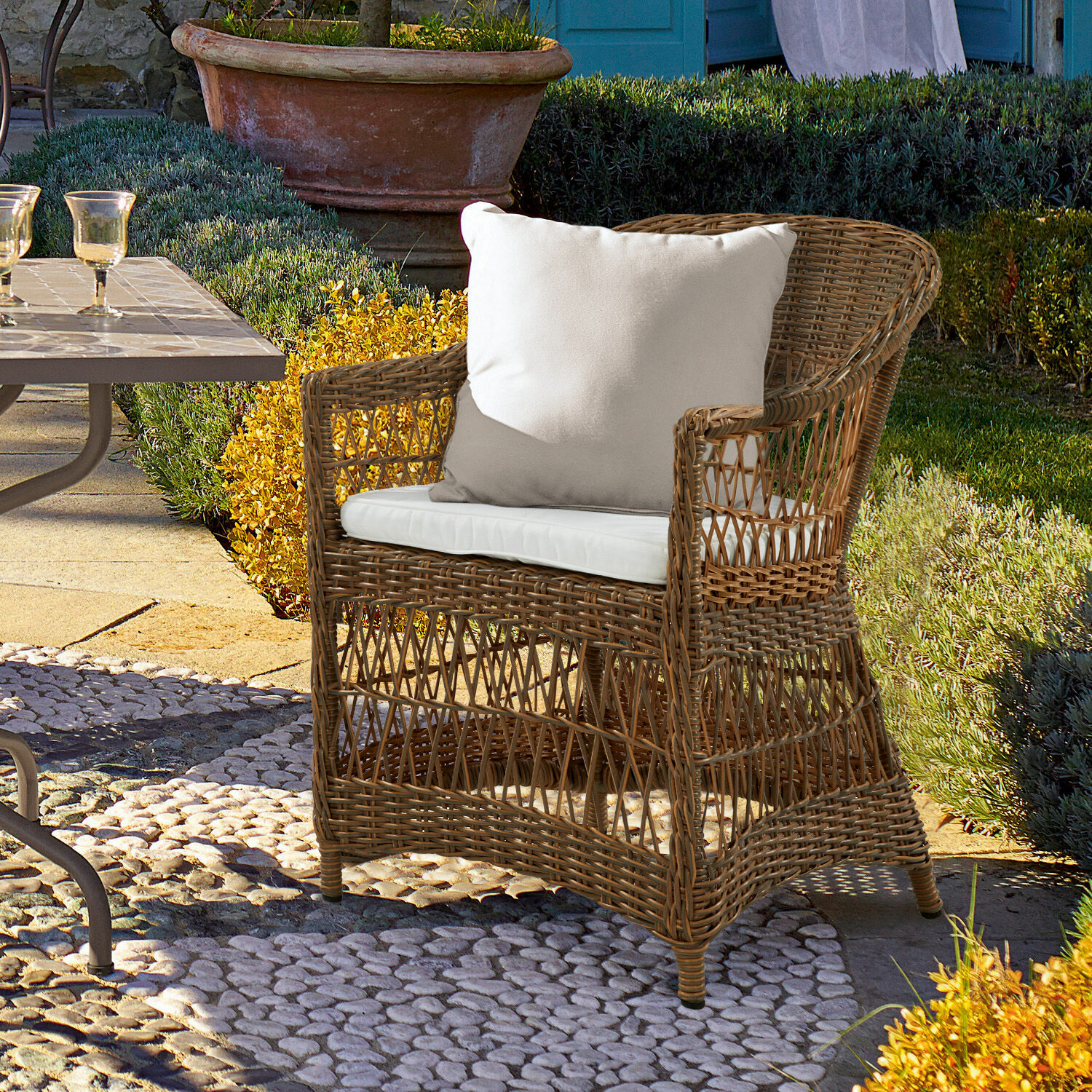 Fauteuil Garden Grove Rotan stoel met wit kussen op stenen terras in tuin, geschikt voor buitenmeubilair