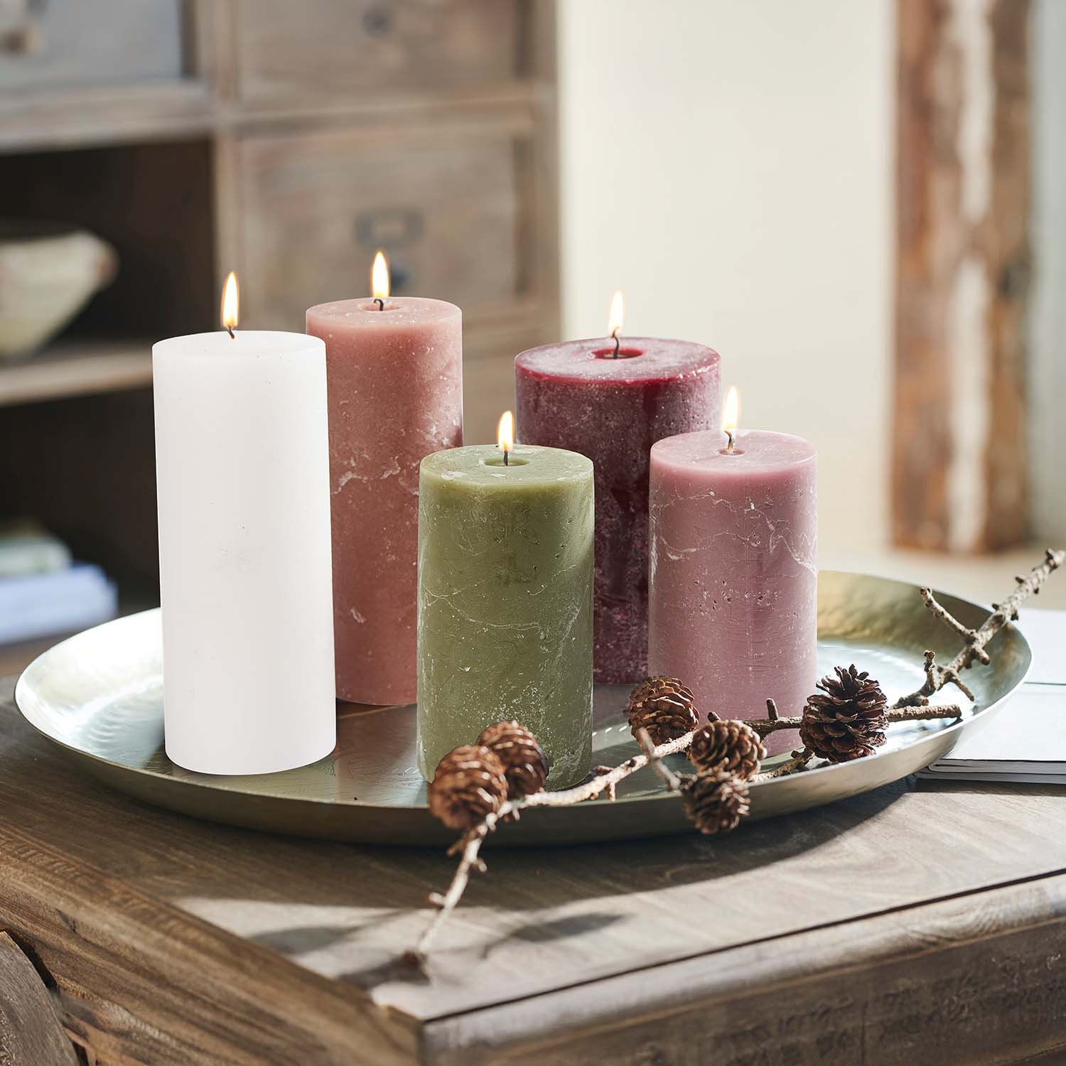 Set van vijf gekleurde kaarsen op een metalen schaal met decoratieve dennenappels op een houten tafel