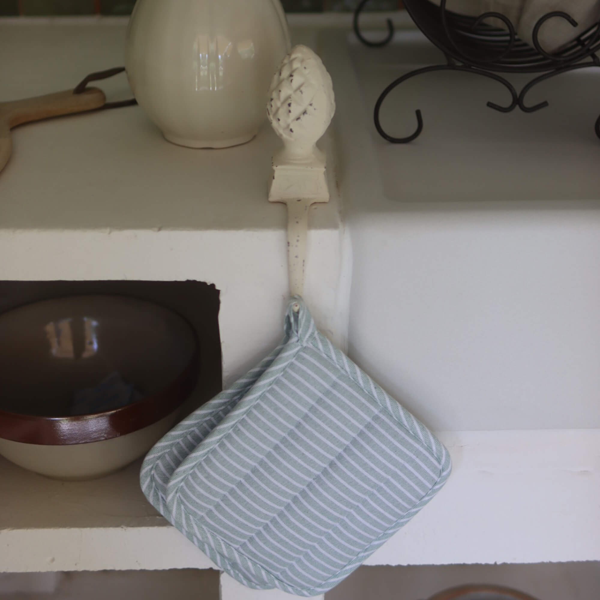 Manique de cuisine en coton rayé vert menthe et blanc suspendue à un crochet en métal dans une cuisine