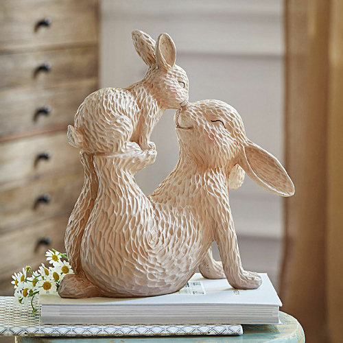 Beige keramieken beeld van twee knuffelende konijnen op boeken, zachte lentebehangdecoratie