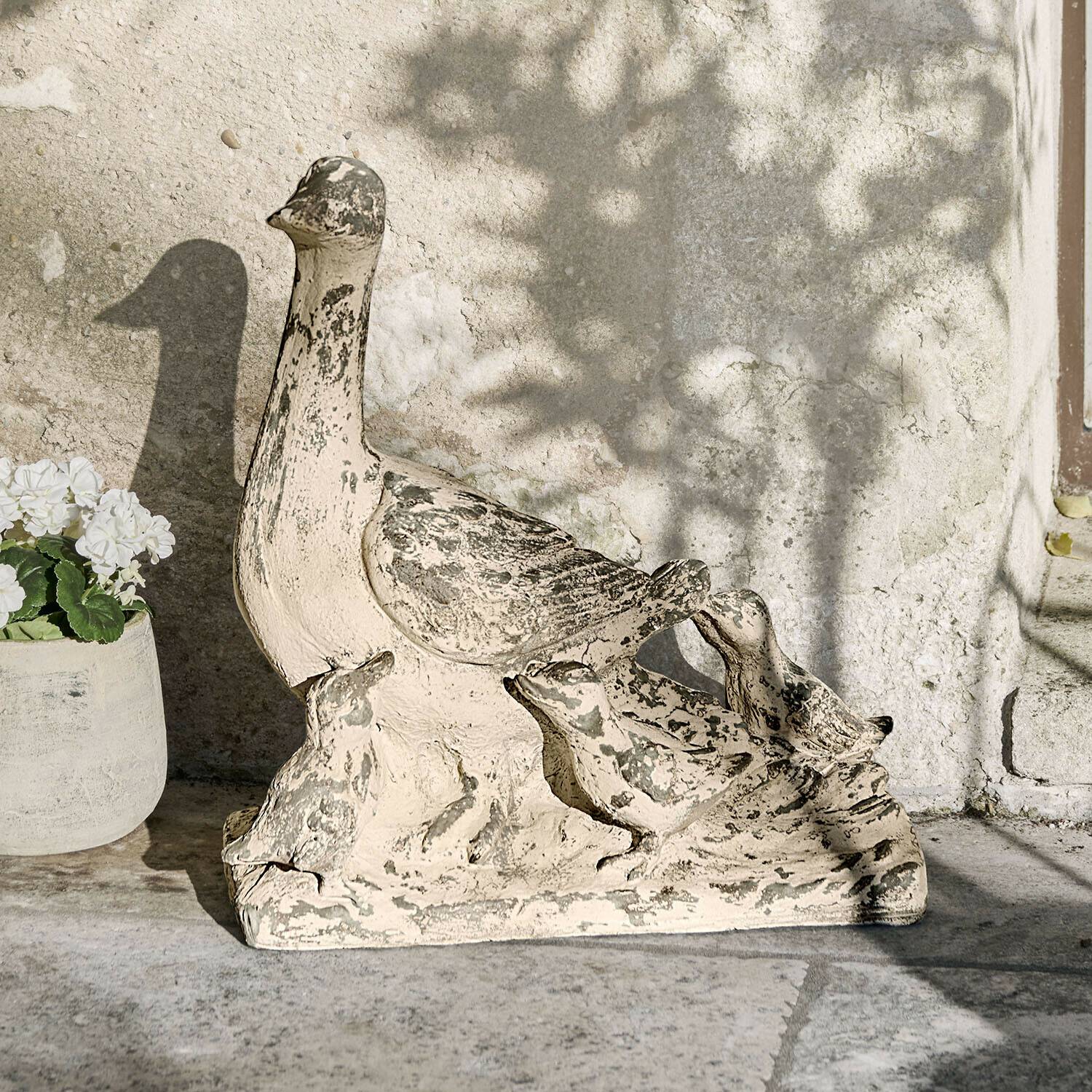 Tuinornament van steen in de vorm van een eend met kuikens in beige en grijs