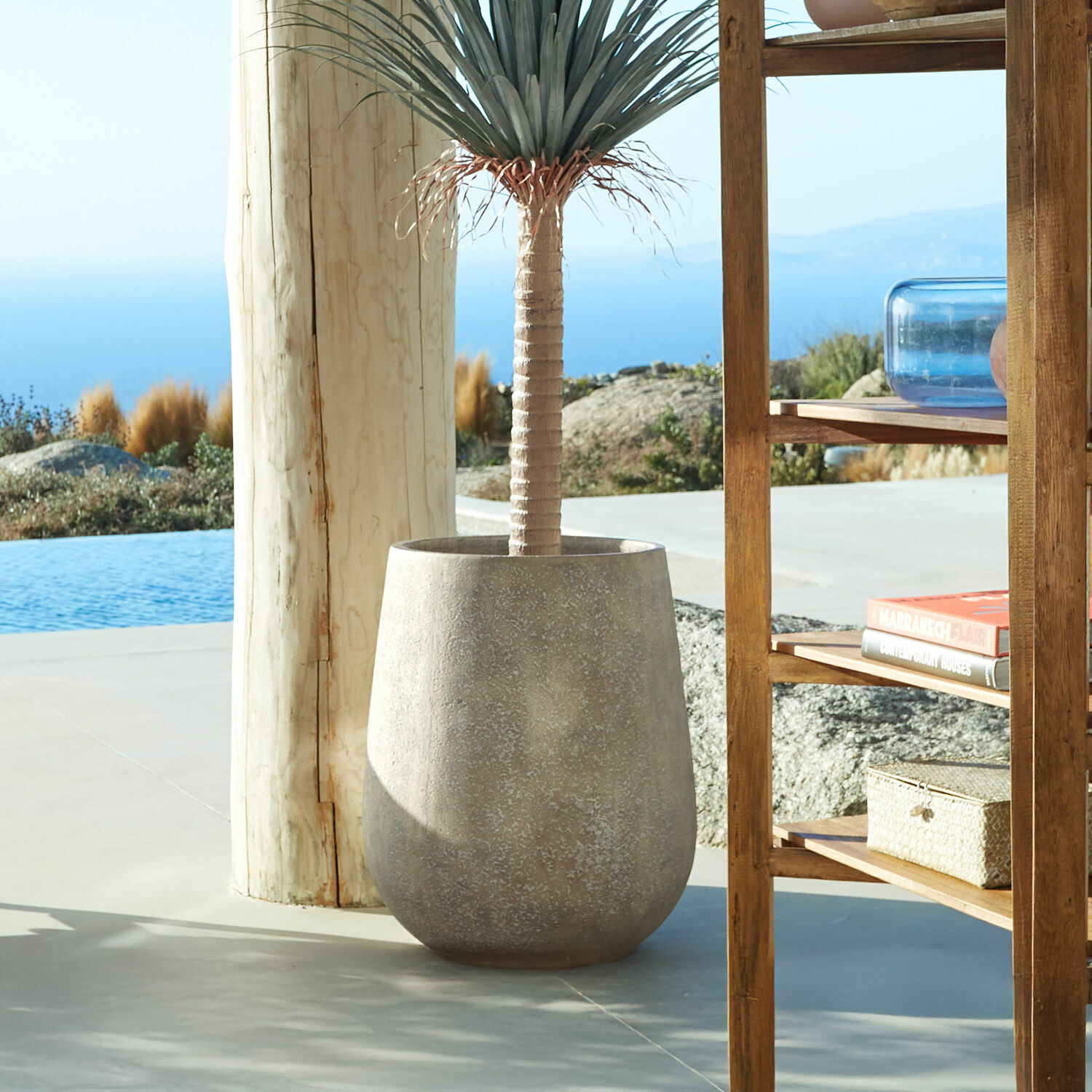 Cache-pot Bressac Grand pot en béton gris avec plante décorative sur terrasse avec vue sur la mer