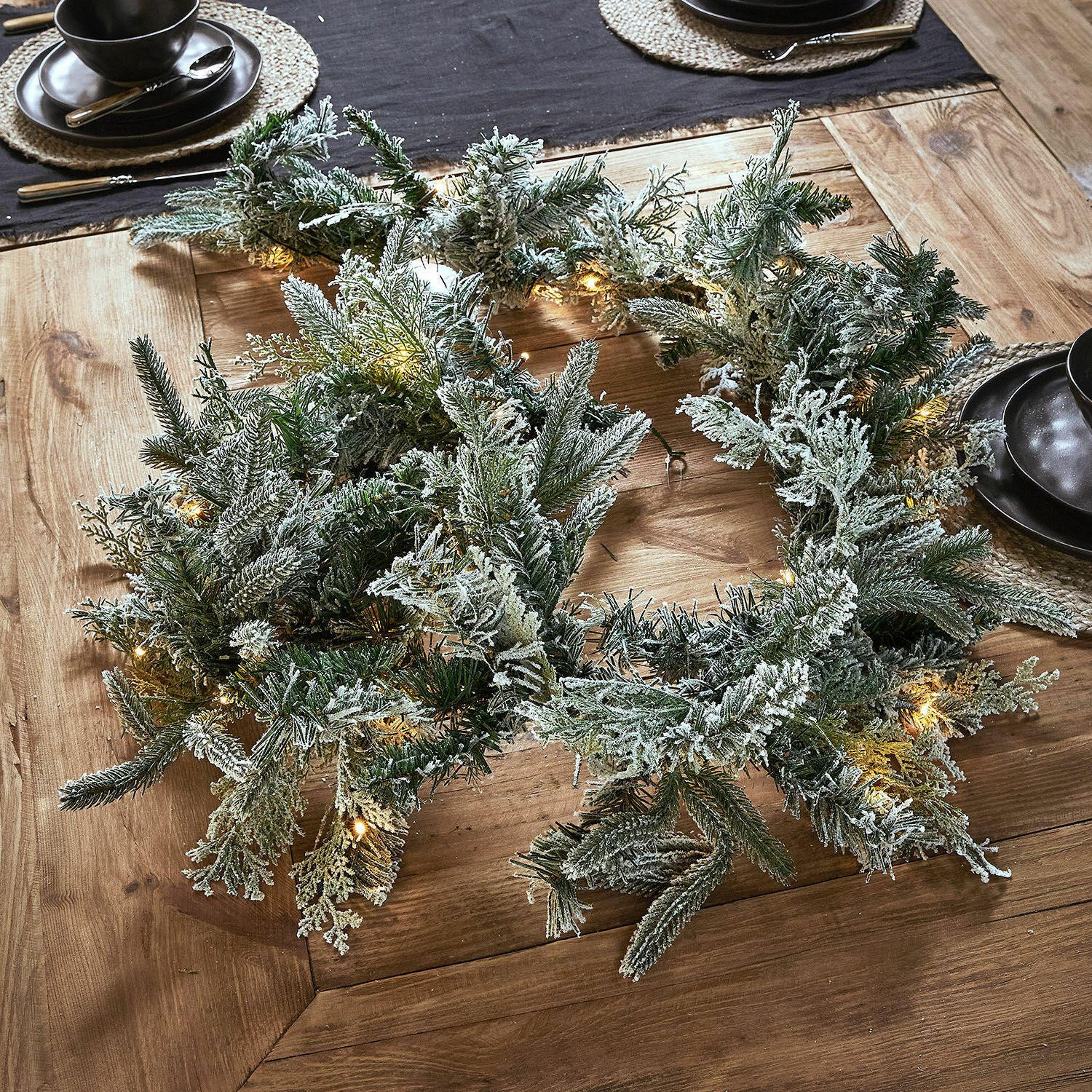 Guirlande LED Cadelise Couronne de Noël enneigée en branches vertes avec éclairage LED doux sur une table en bois