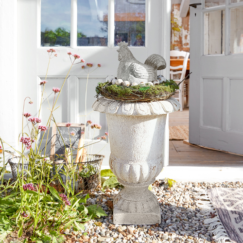 Decoratieve witte stenen vaas met kipfiguur en nest met eieren buiten bij de deur