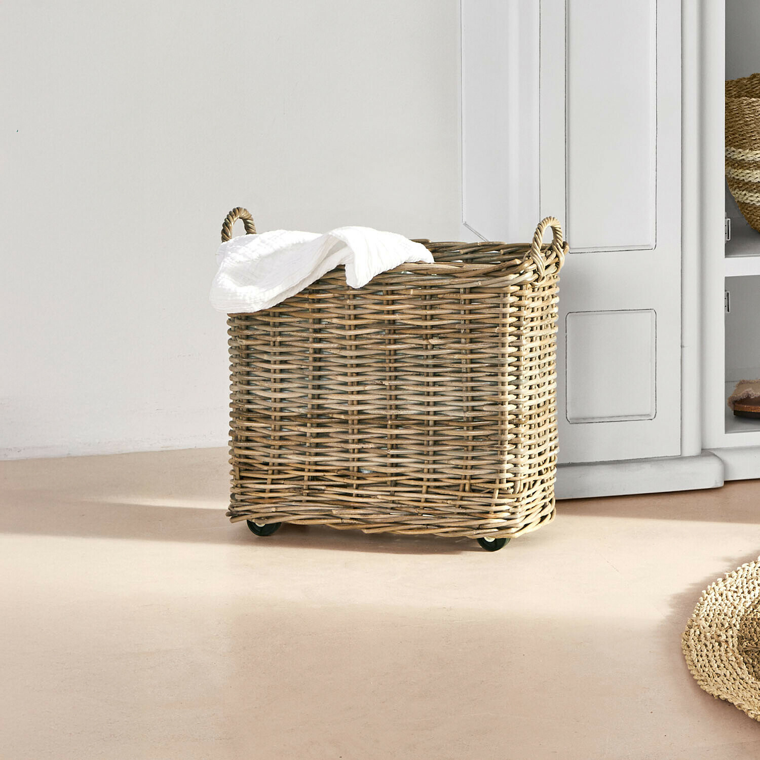Panier à linge en osier naturel sur roulettes avec serviette blanche dans une pièce lumineuse
