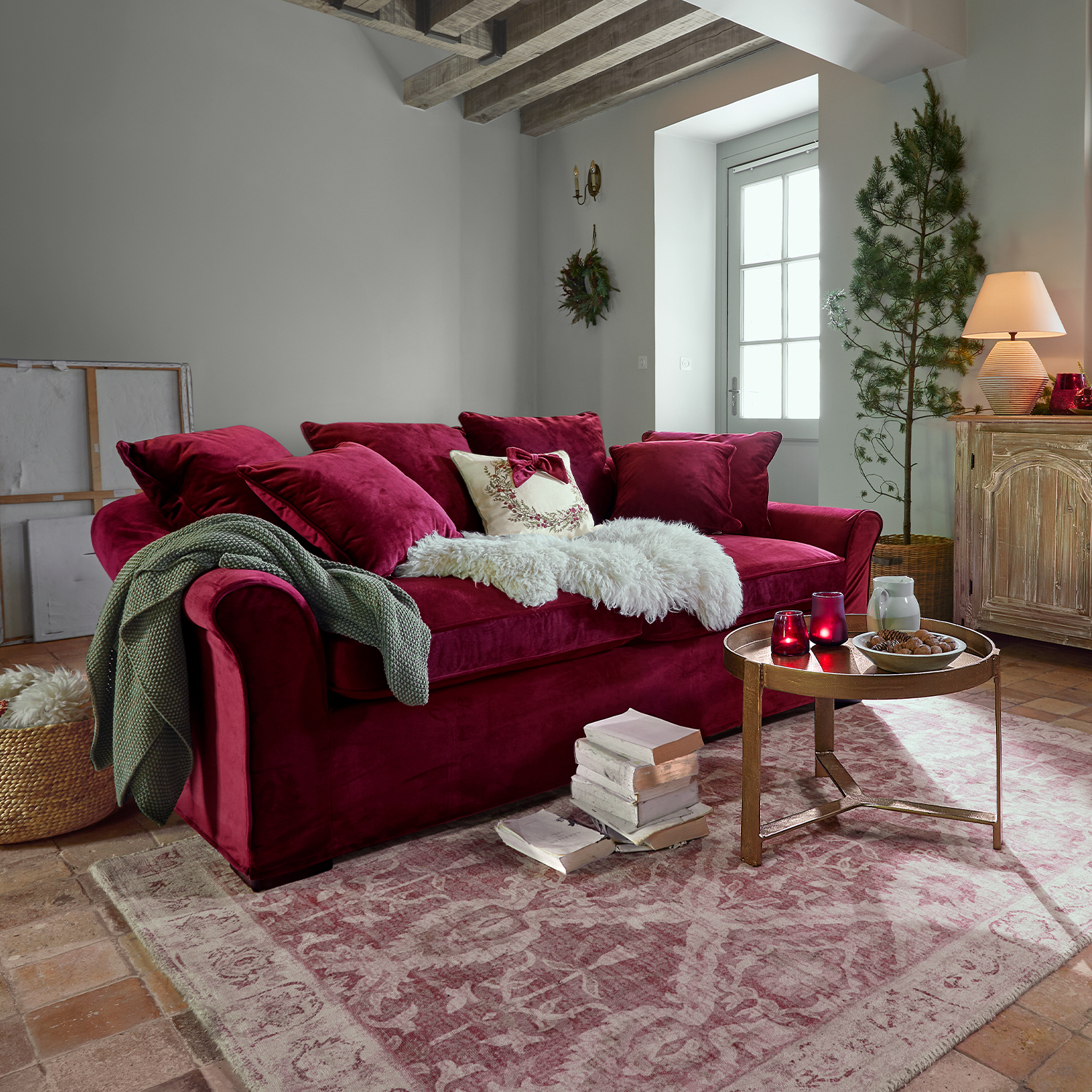 Canapé rouge en velours avec coussins et plaid doux dans un salon chaleureux avec escalier en bois