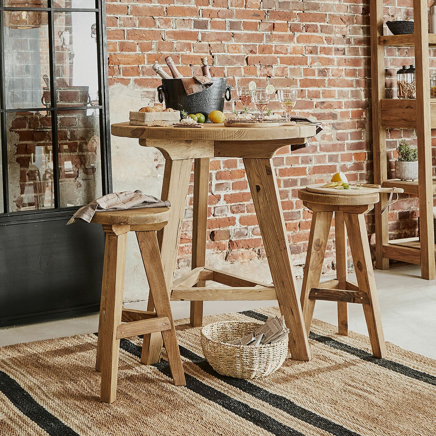 Table haute en bois naturel avec deux tabourets assortis sur tapis en jute dans un intérieur industriel