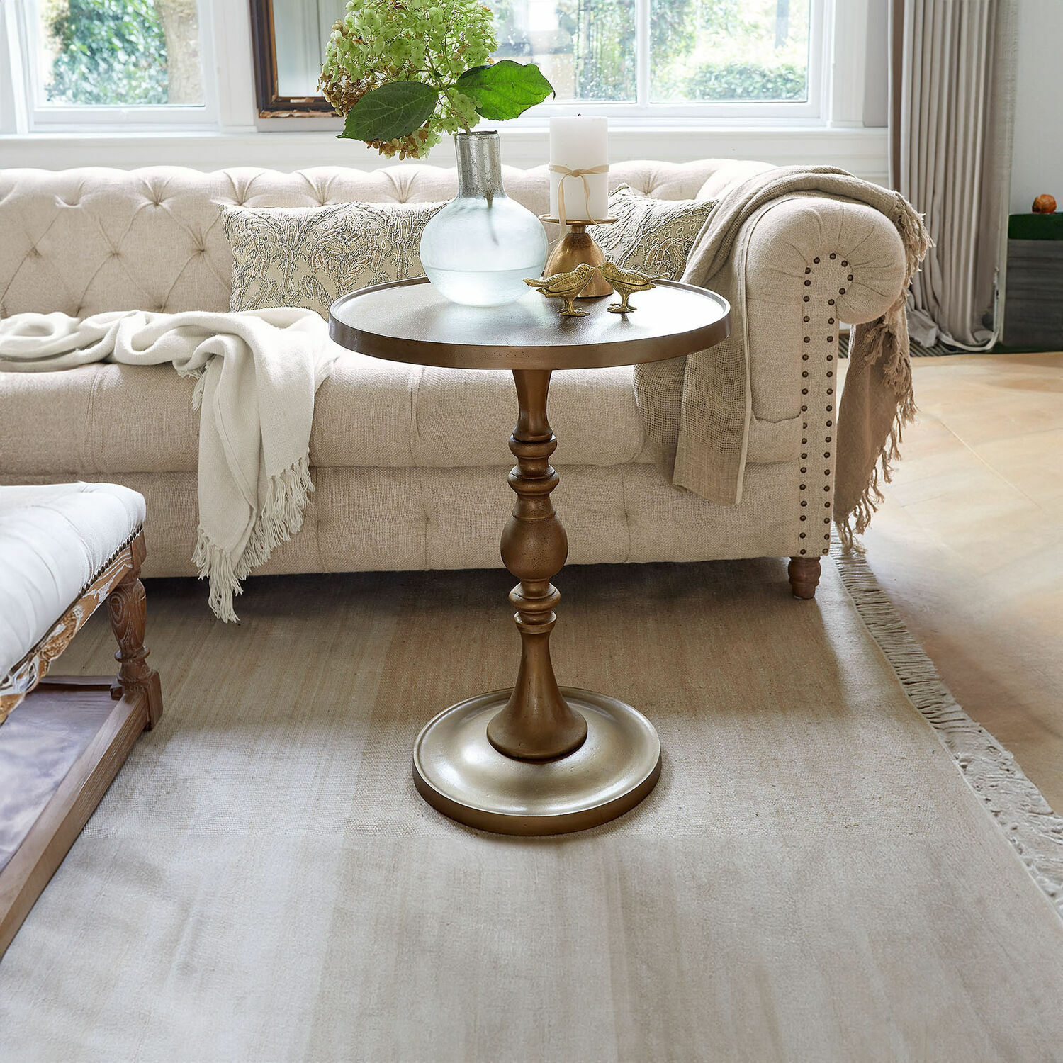 Guéridon Uralive Table d'appoint ronde en métal couleur laiton devant un canapé beige avec décorations dans un salon