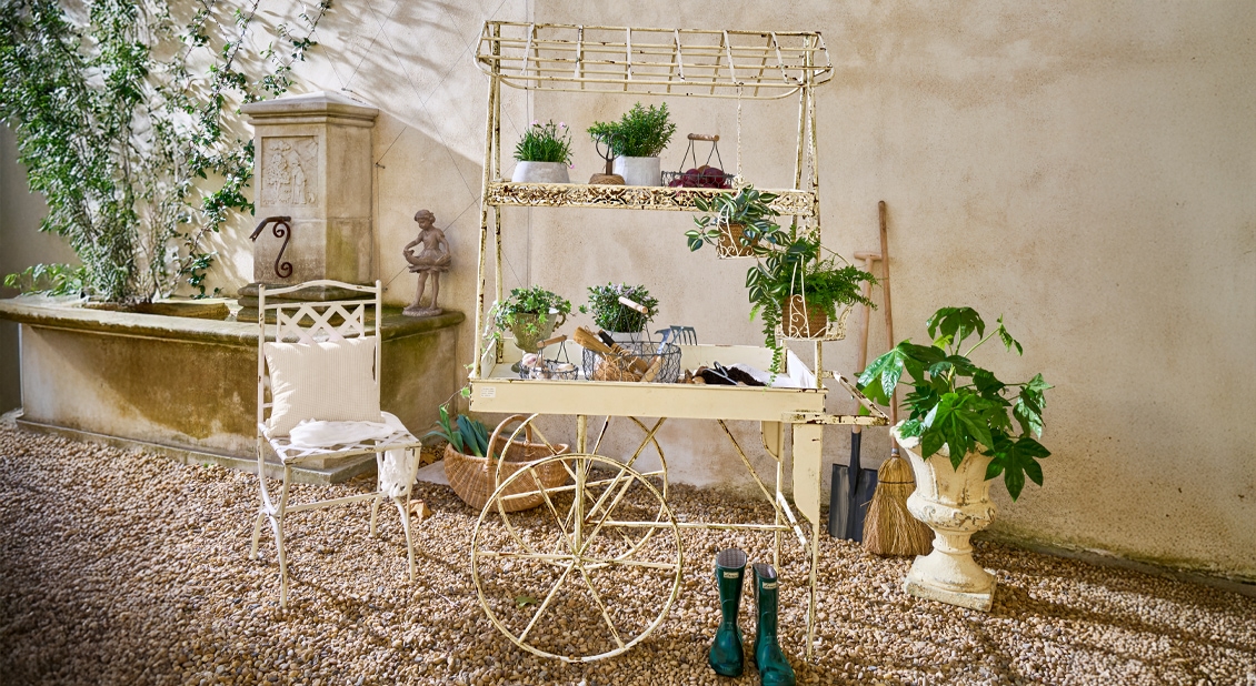 Franse tuinwagen van metaal met groene planten en tuingereedschap op grindgrond in tuin