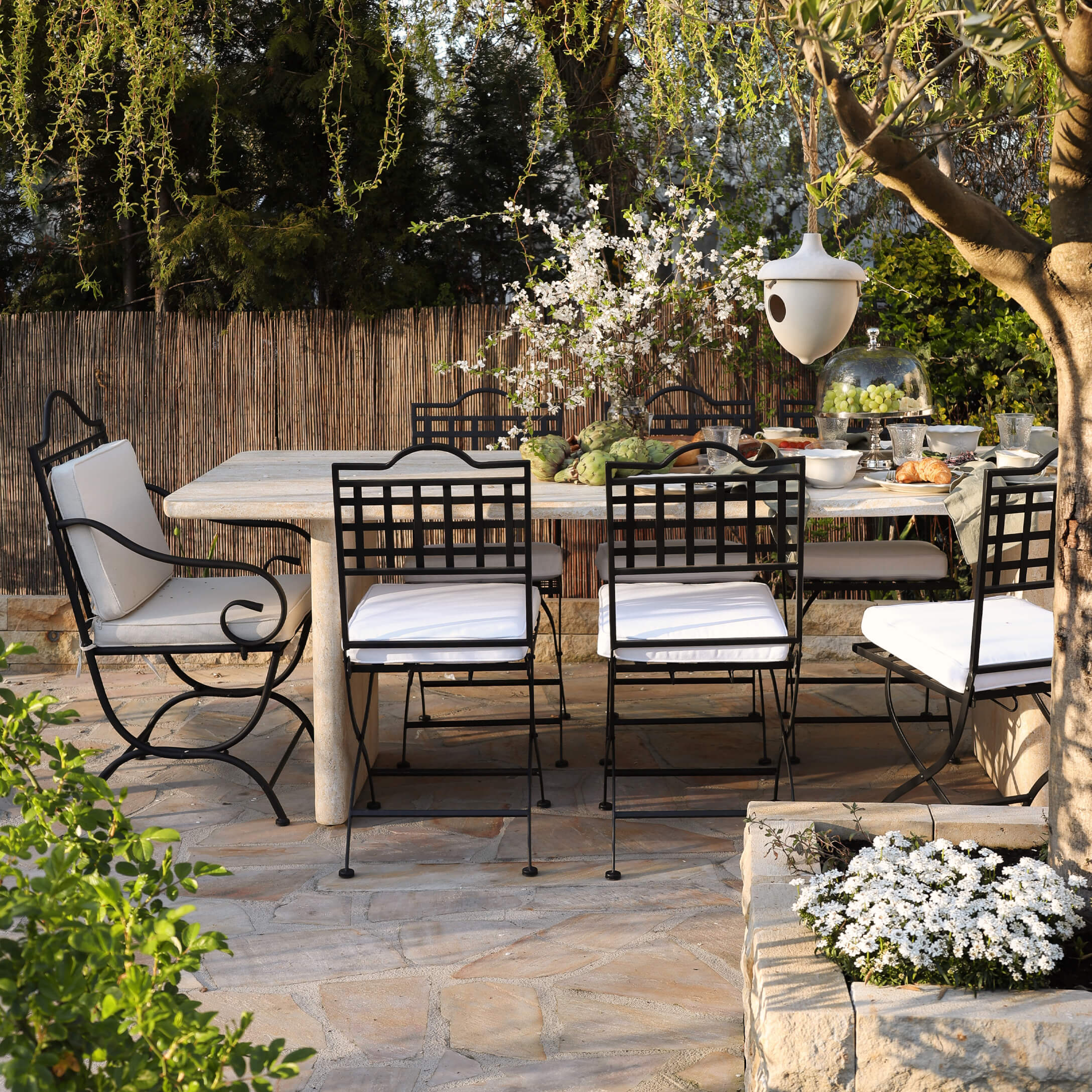 Tuinmeubelset met zwarte metalen stoelen en lichte stenen tafel op zonnig terras