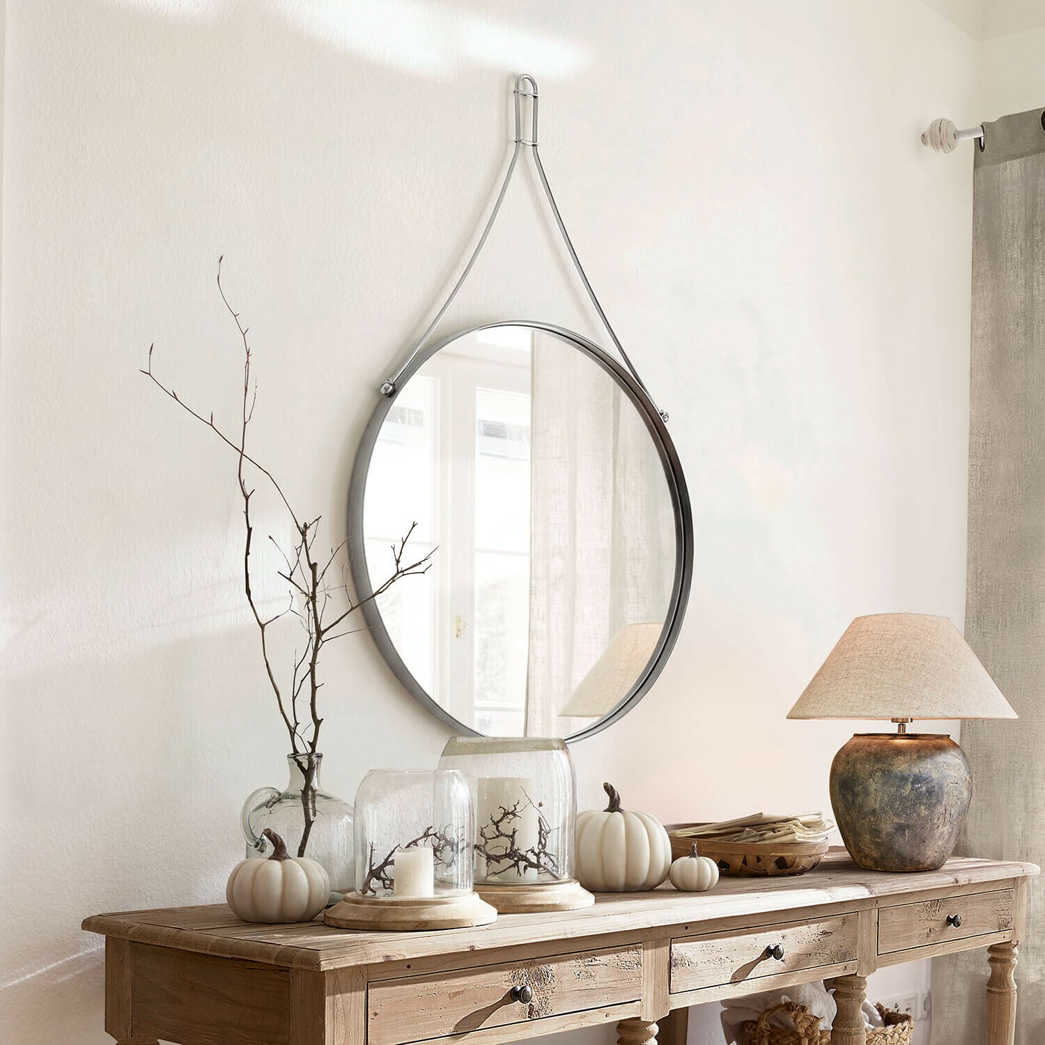 Miroir Célivaux Miroir rond suspendu avec sangle métallique argentée au-dessus d'une console en bois décorée
