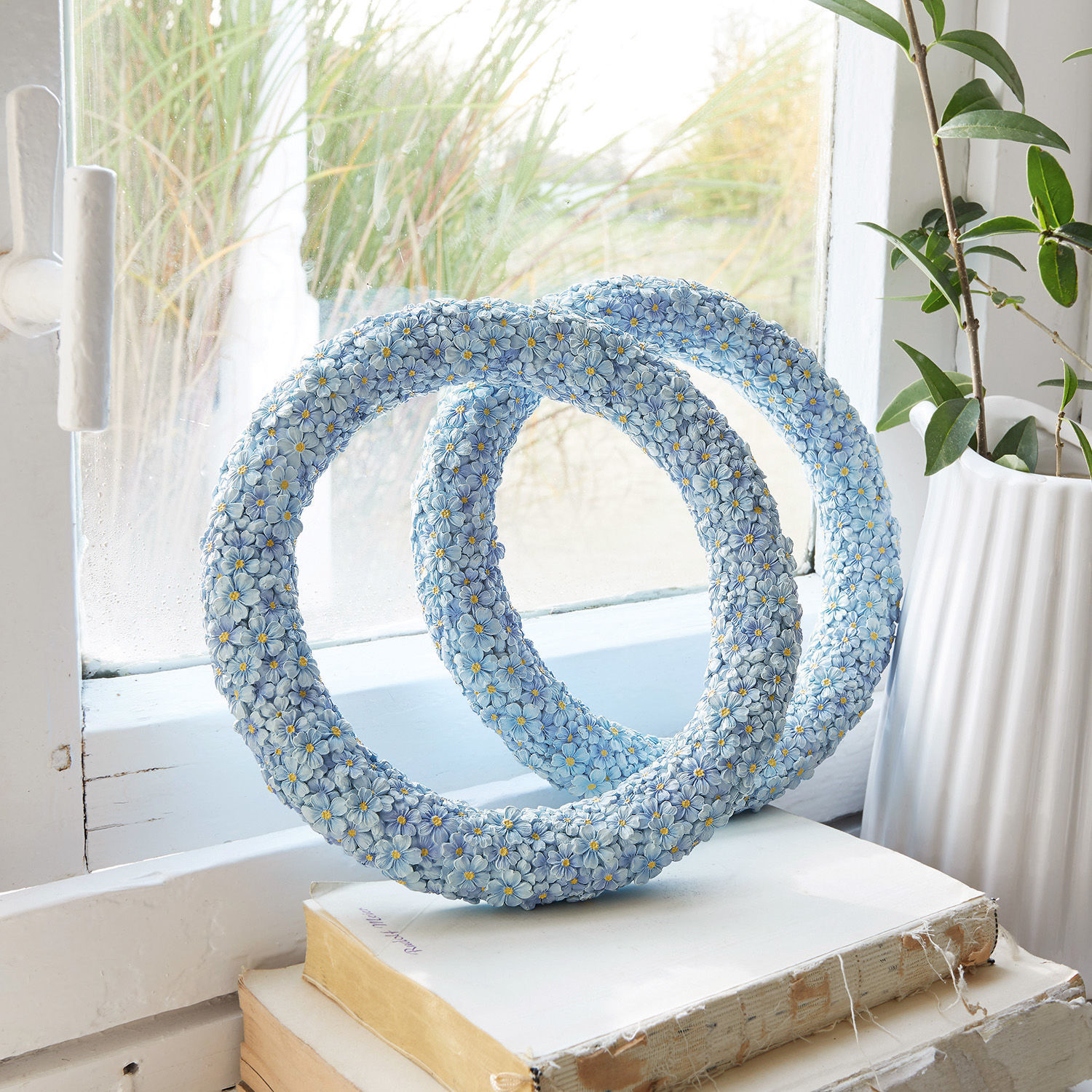 Sculpture décorative bleue en résine avec fleurs posée sur des livres près d'une fenêtre, décoration intérieure