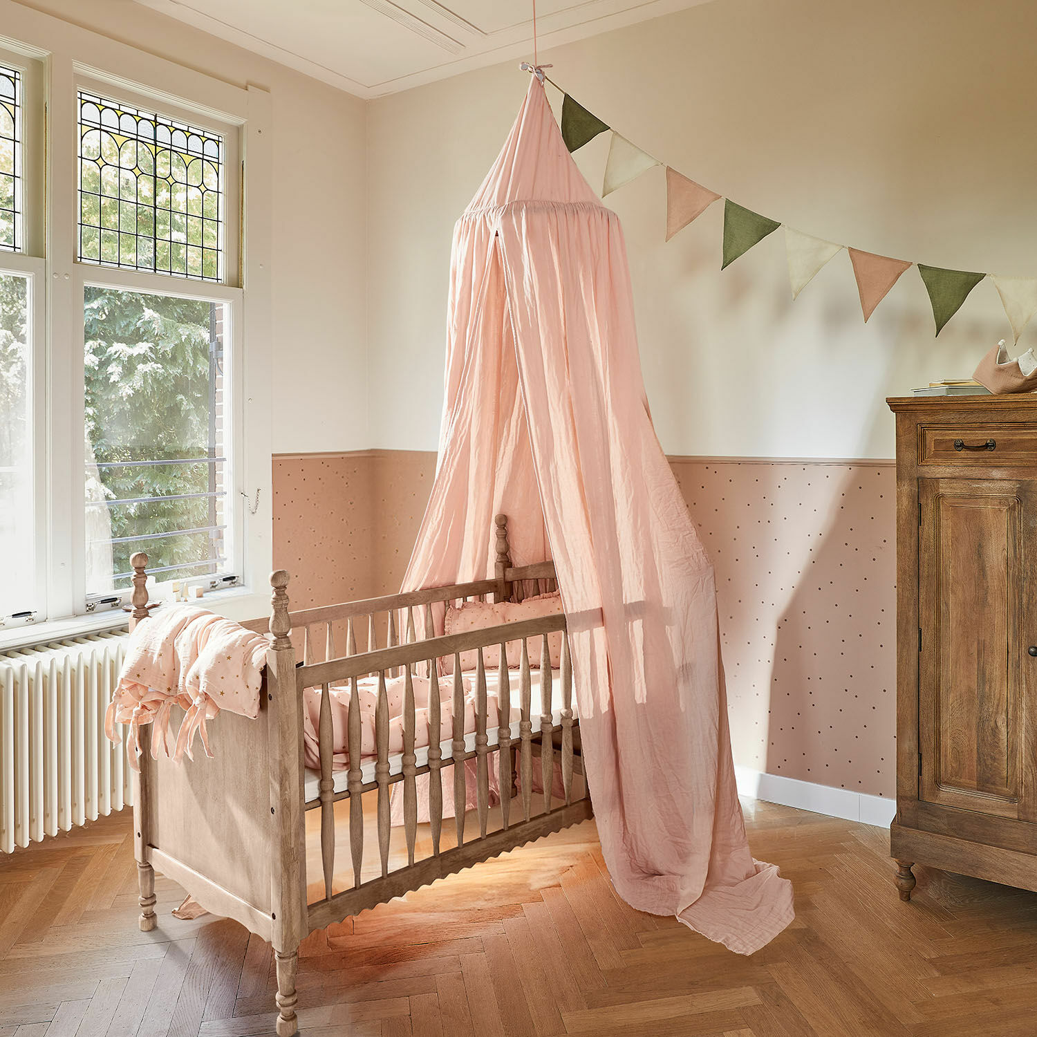 Ledikant Merveillon Houten babybed met roze hemel en bijpassend beddengoed in pastelkleurige kinderkamer