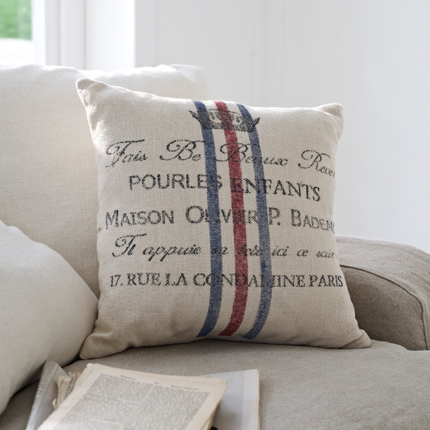 Beige sierkussen van stof met print en rood-blauwe strepen op lichte bank in woonkamer