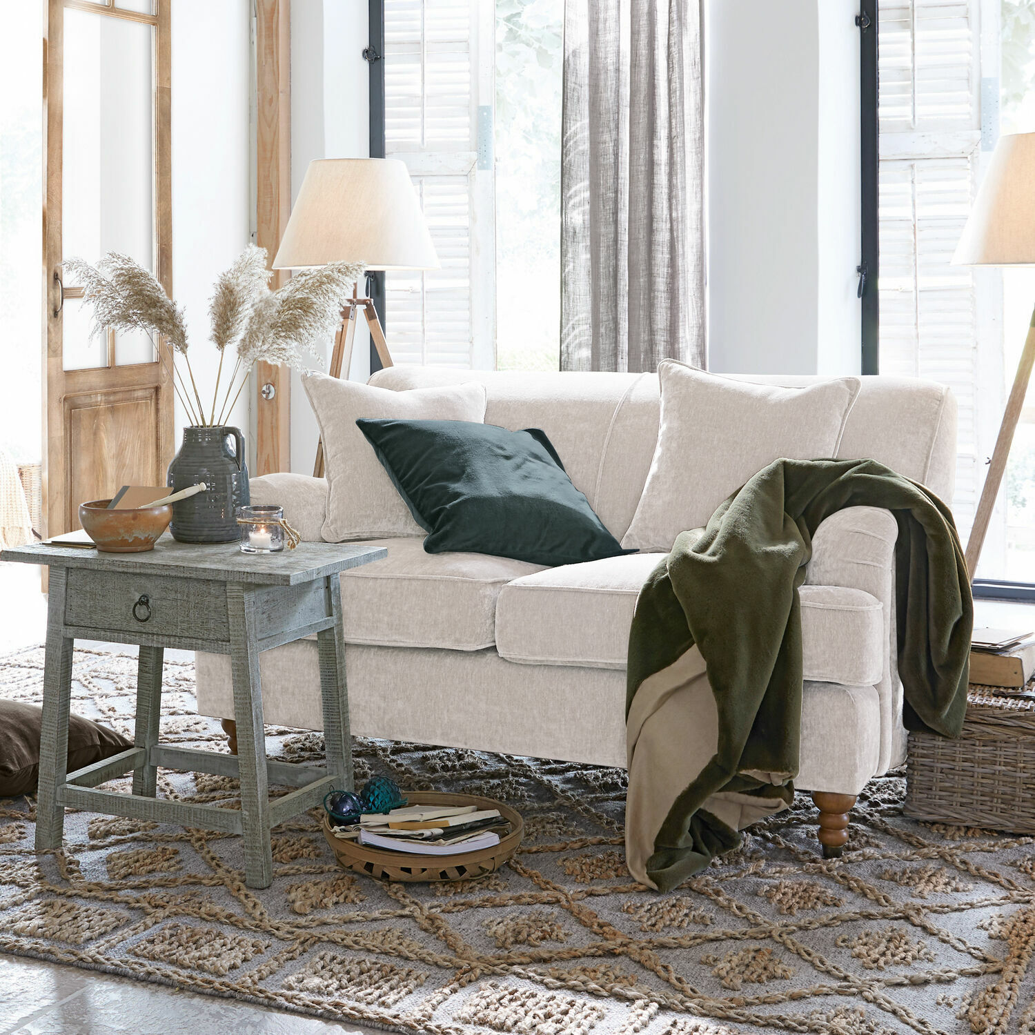 Canapé beige en tissu doux avec couverture verte et coussin dans un salon chaleureux avec table en bois