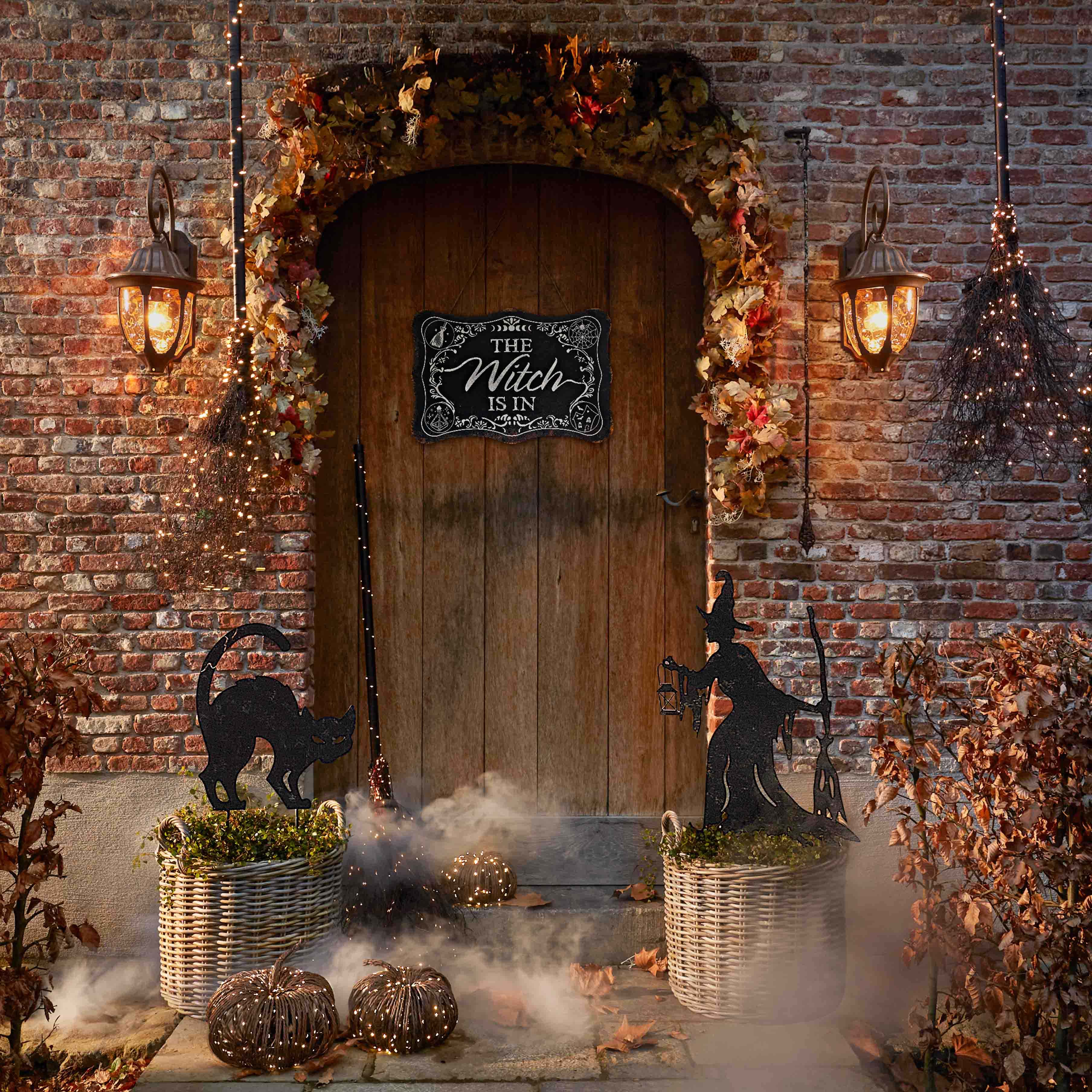 Halloweenversiering met zwarte kat, heks en lantaarns bij houten deur en bakstenen muur