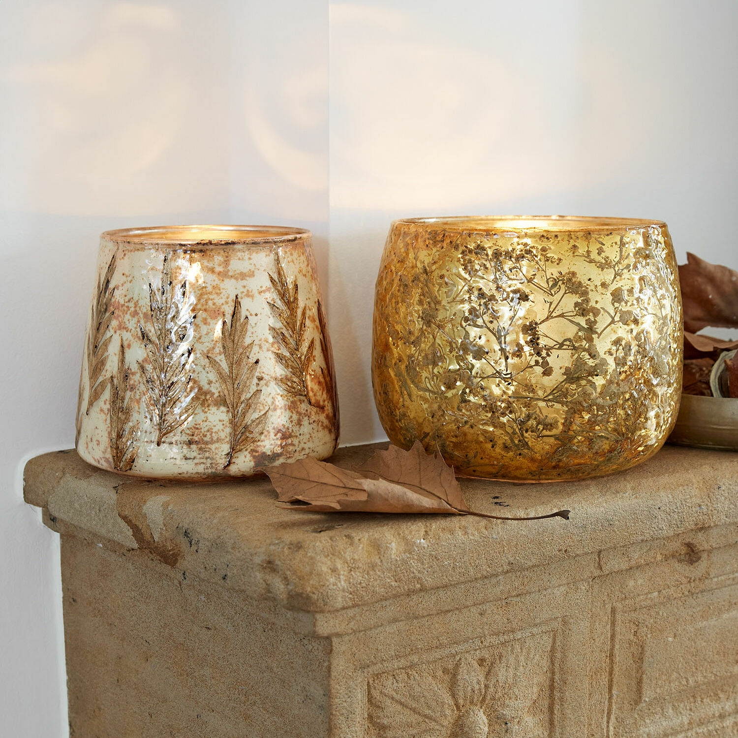 Windlicht set van 2 Hivalen Twee decoratieve glazen windlichten met bladmotief in goud en crème op een stenen plank