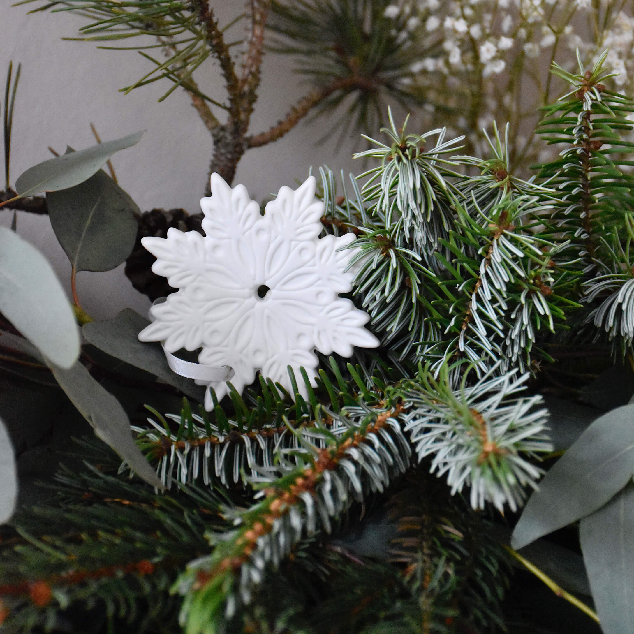 Décoration de Noël en céramique blanche en forme de flocon de neige sur branches de sapin vertes