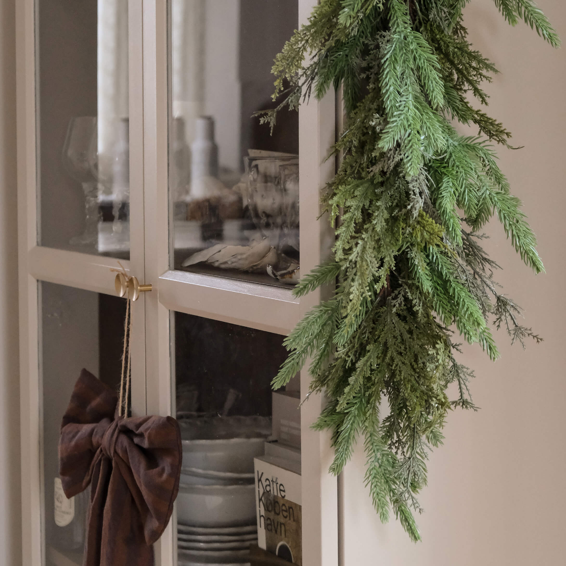 Guirlande verte décorative en branches suspendue sur une armoire claire avec portes vitrées style scandinave