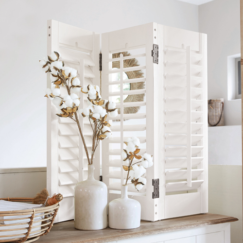 Witte houten kamerscherm met lamellen op tafel, versierd met katoenen bloemen, rustieke stijl