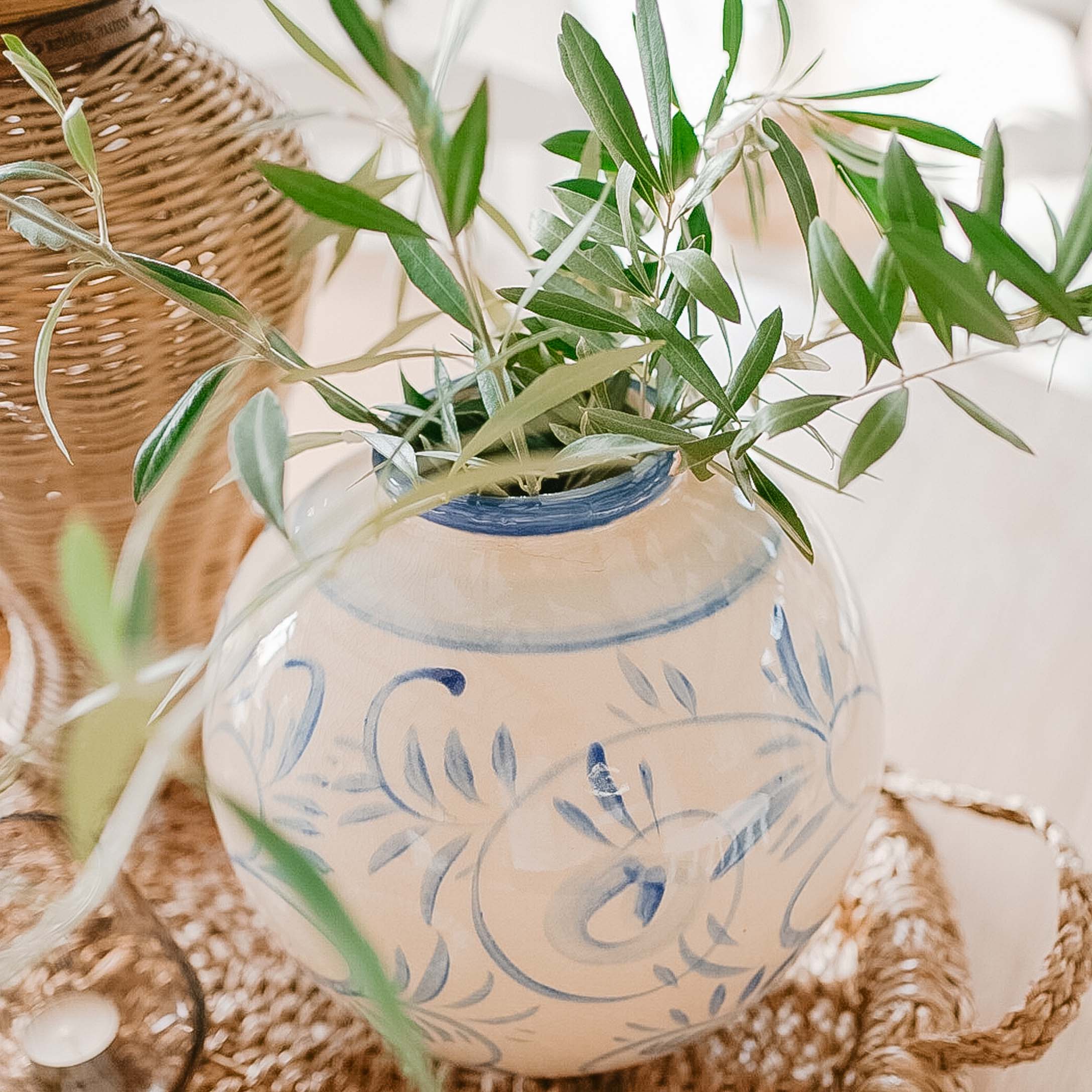 Vase en céramique blanche avec motif bleu et feuillage vert sur fond en osier pour décoration