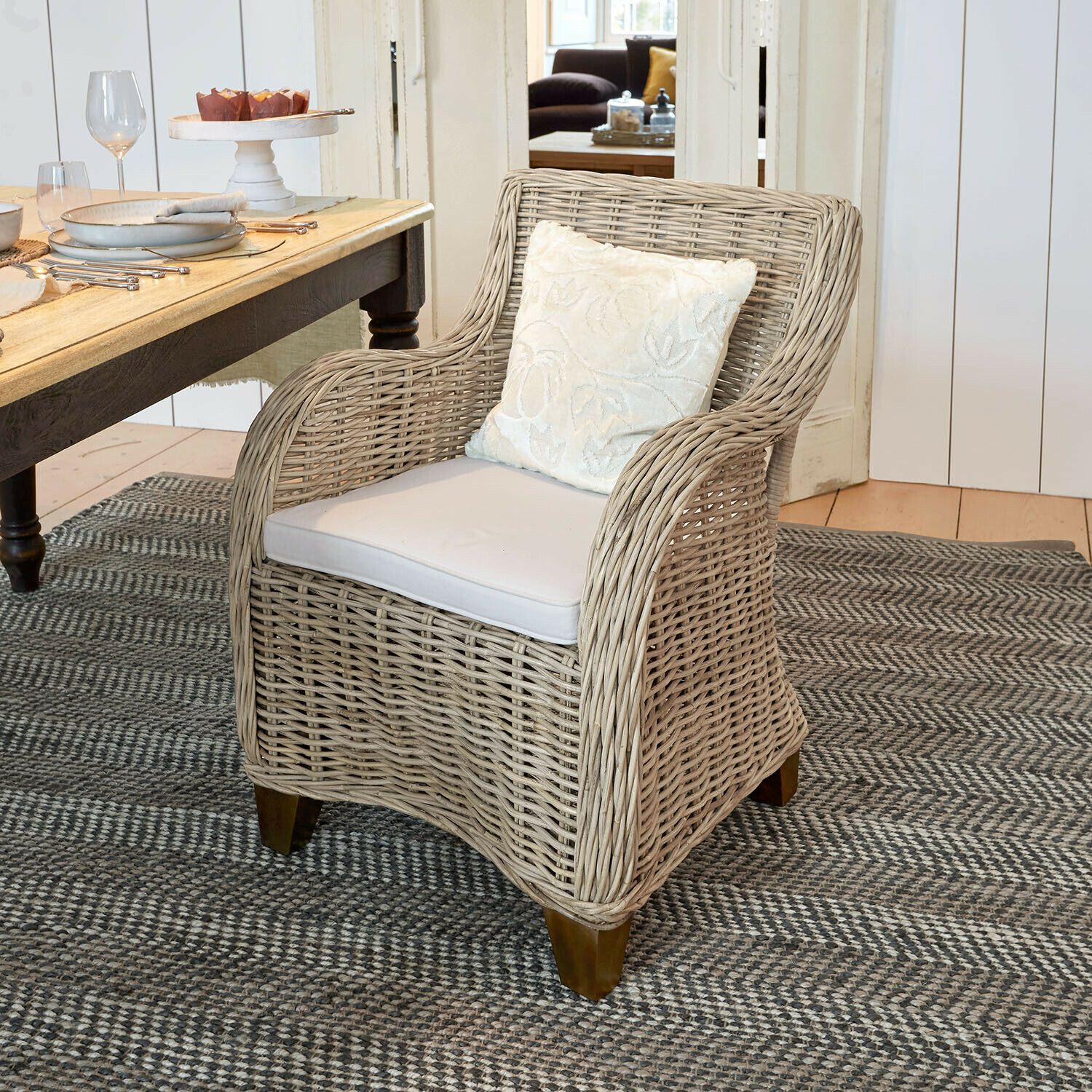 Stoel Penrosse Beige rotan fauteuil met wit kussen op grijs tapijt in eetkamer