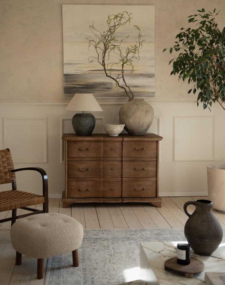 Commode en bois naturel à six tiroirs avec vases décoratifs et lampe dans un salon élégant
