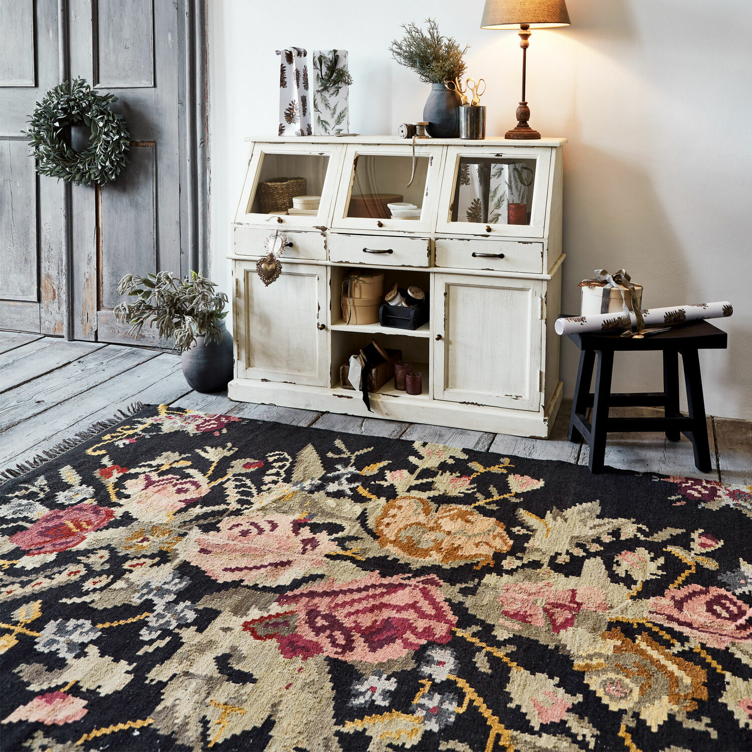 Tapis Matteo Tapis à motif floral foncé devant un buffet en bois blanc vieilli avec décoration vintage et lampe