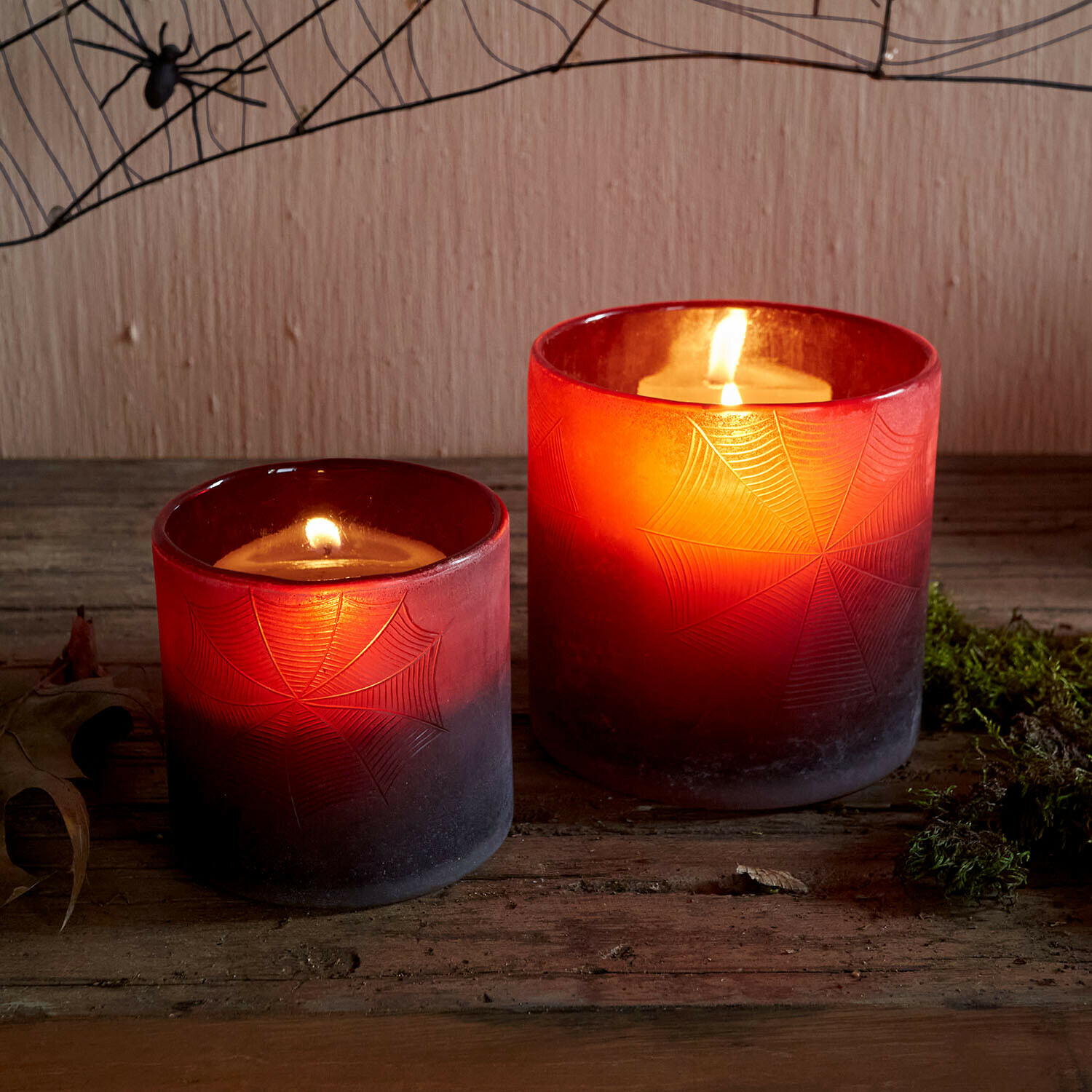 Windlicht set van 2 Brannora Twee rode glazen windlichten met spinnenwebmotief, brandende kaarsen op houten tafel
