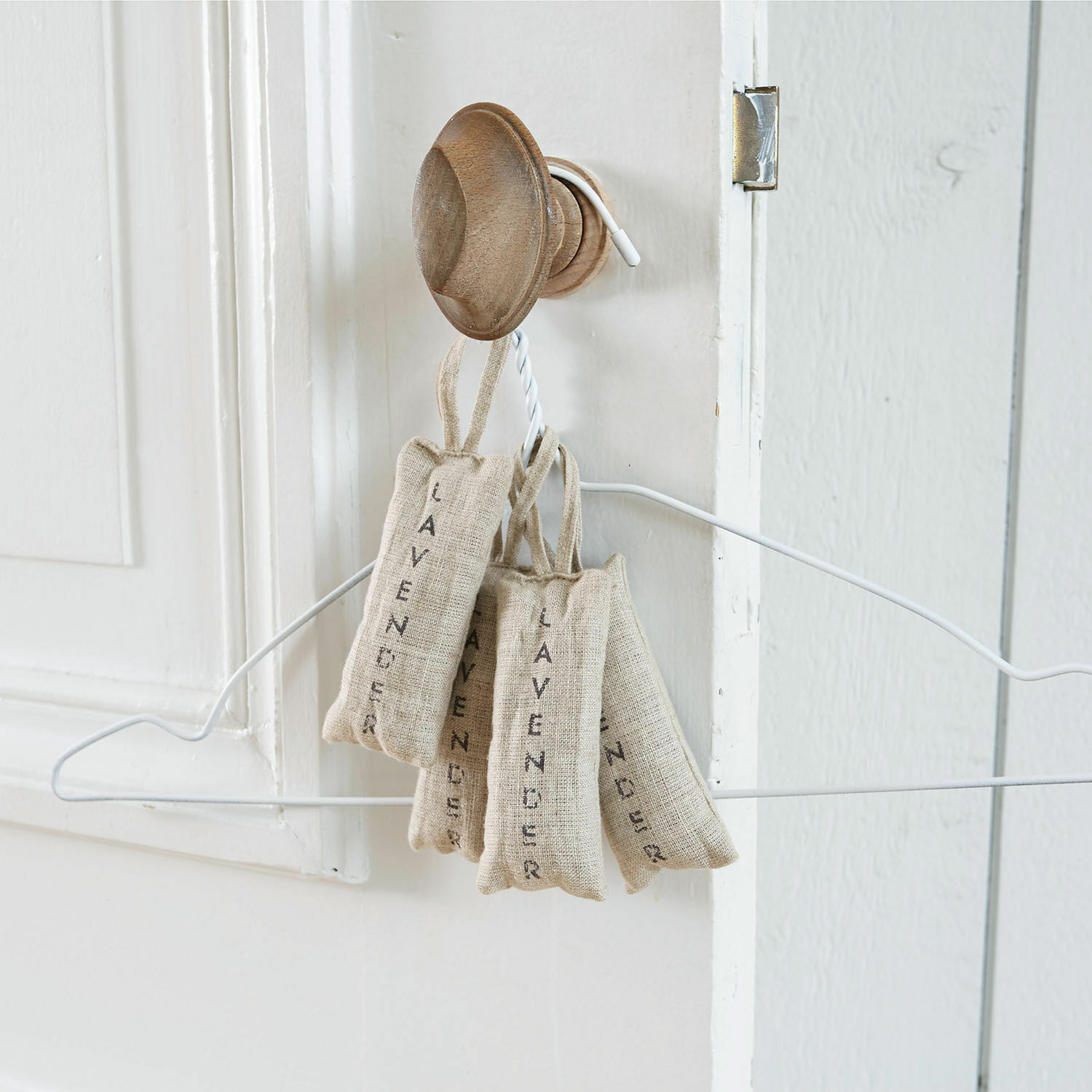 Sachets en lin naturel remplis de lavande suspendus à un crochet en bois sur une porte blanche