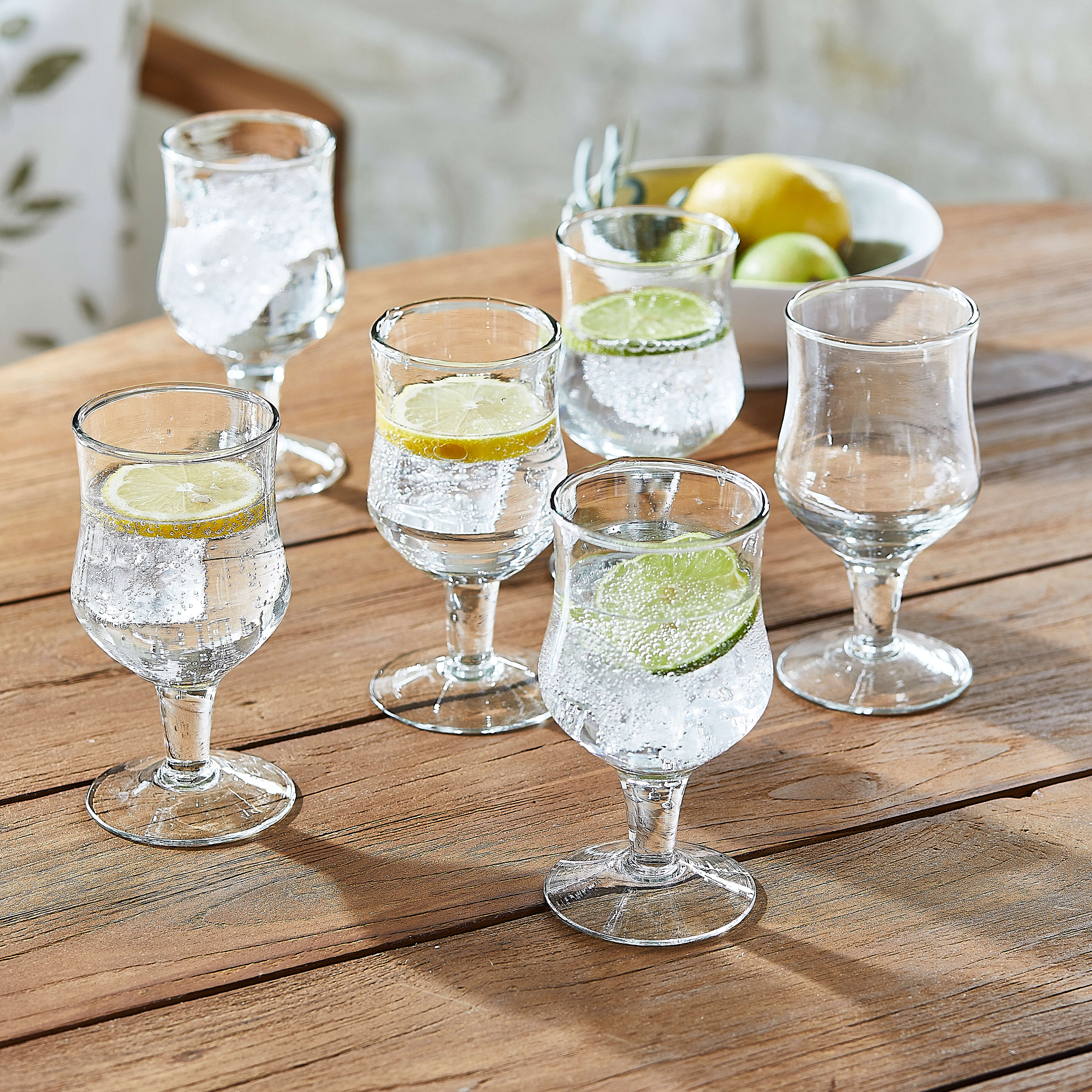 Set van zes transparante glazen met water en schijfjes citroen en limoen op houten tafel