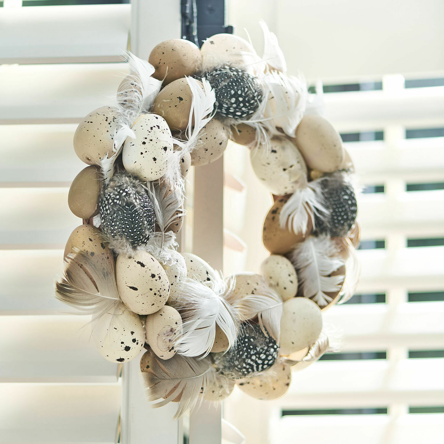 Couronne décorative avec plumes beiges et noires et œufs artificiels pour décoration printanière