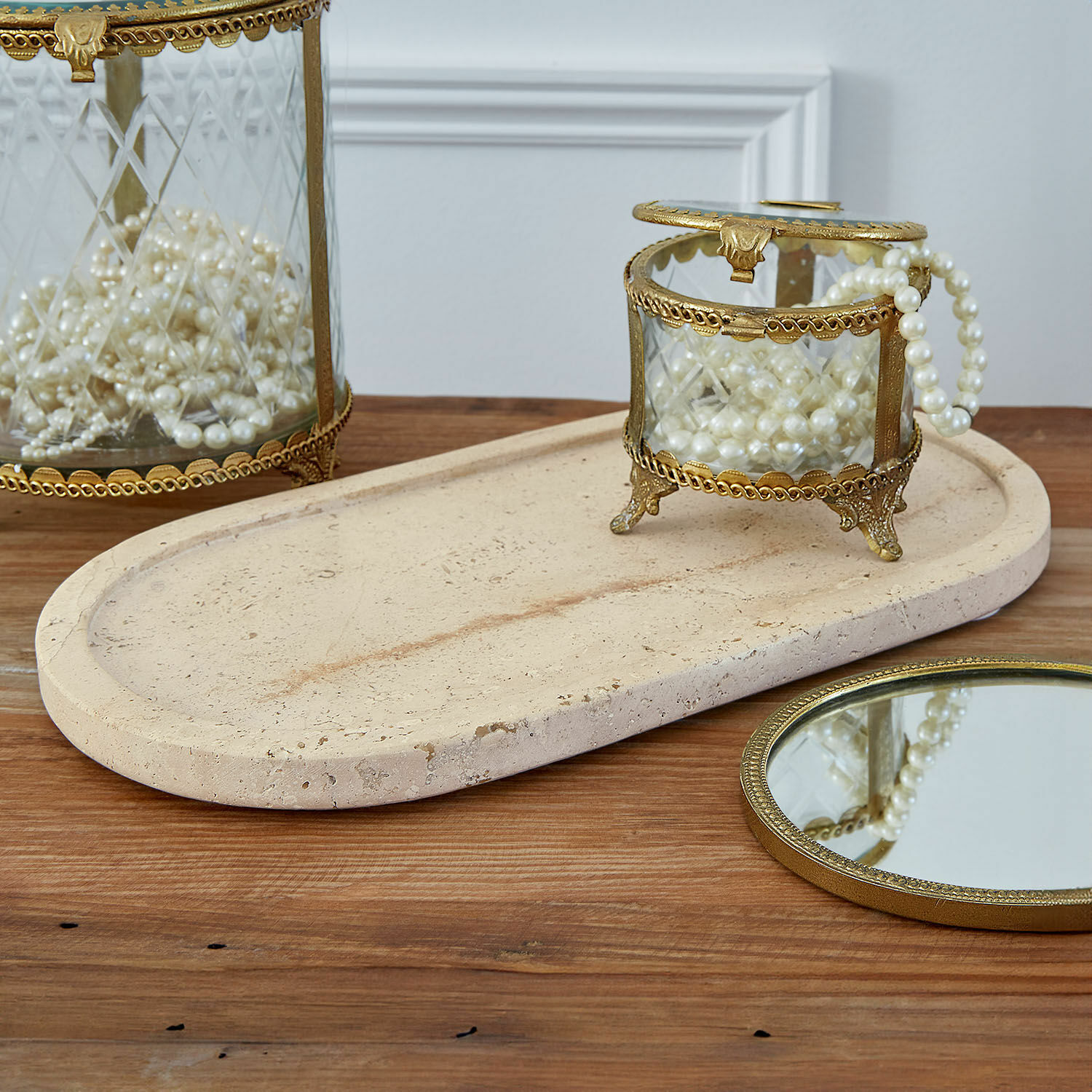 Schaal Thalina Glazen sieradendoos met messing frame en parels op beige stenen dienblad op houten tafel
