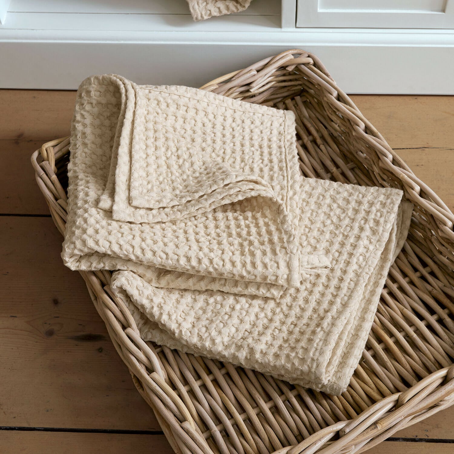Serviette beige en coton gaufré posée dans un panier en osier sur un sol en bois
