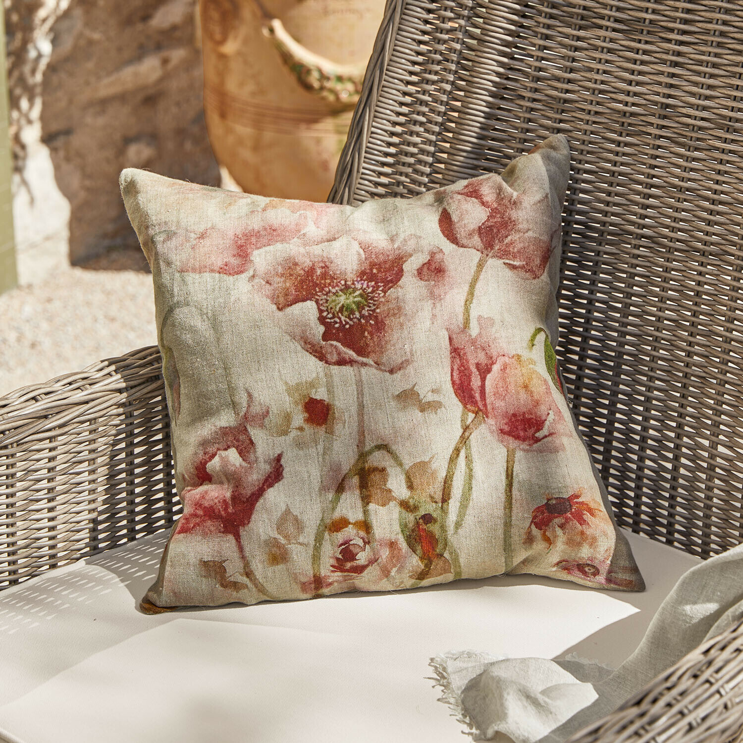 Housse de coussin Garavine Coussin décoratif en lin avec motif floral rouge posé sur un fauteuil en osier beige