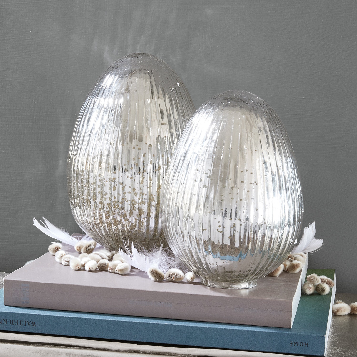 Paasei set van 2 Duvera Twee decoratieve zilverkleurige glazen kandelaars op boeken, versierd met veren en katjes