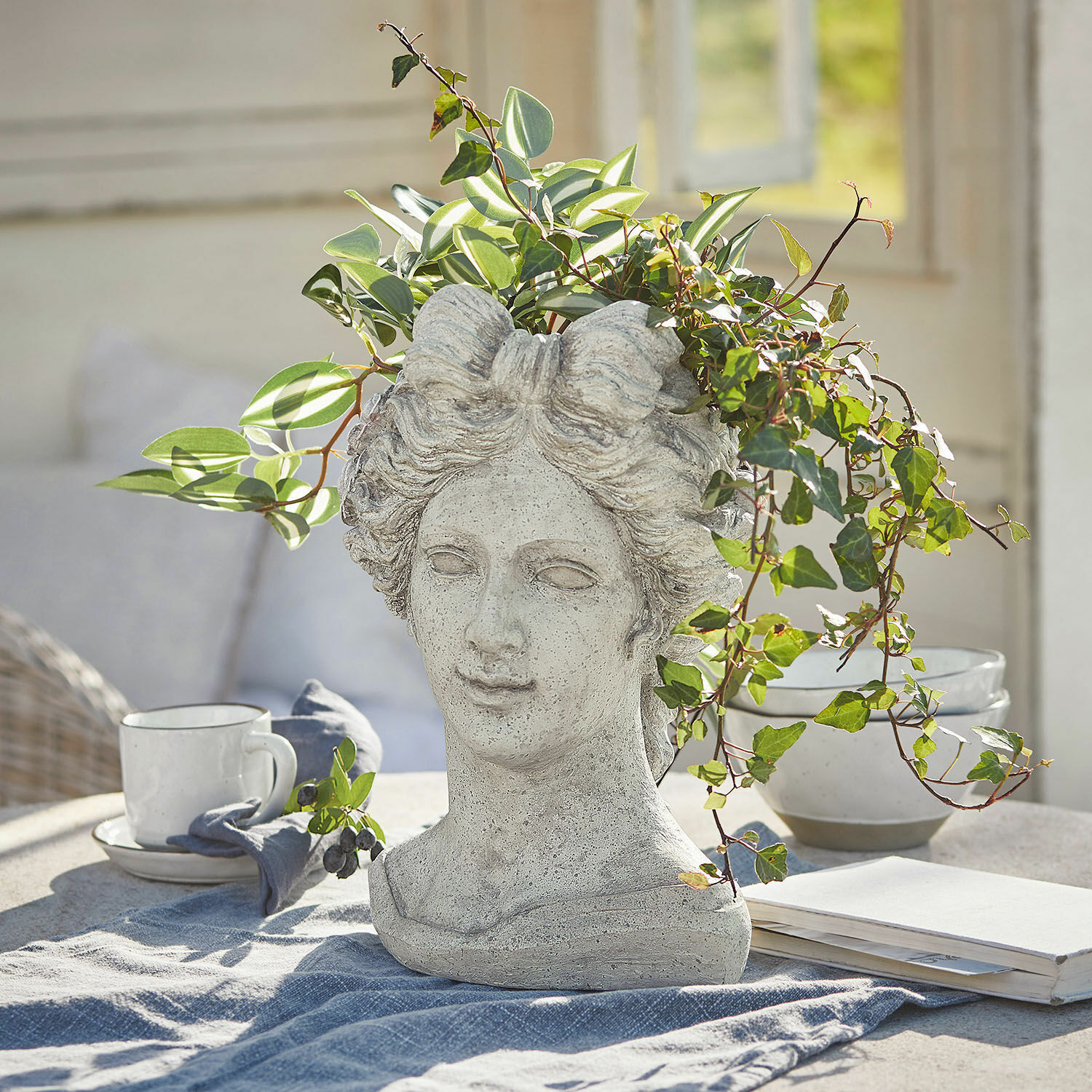 Sierpot Cassiopeia Bloempot in de vorm van een vrouwenhoofd van grijs steen met groene planten op een lichte tafel