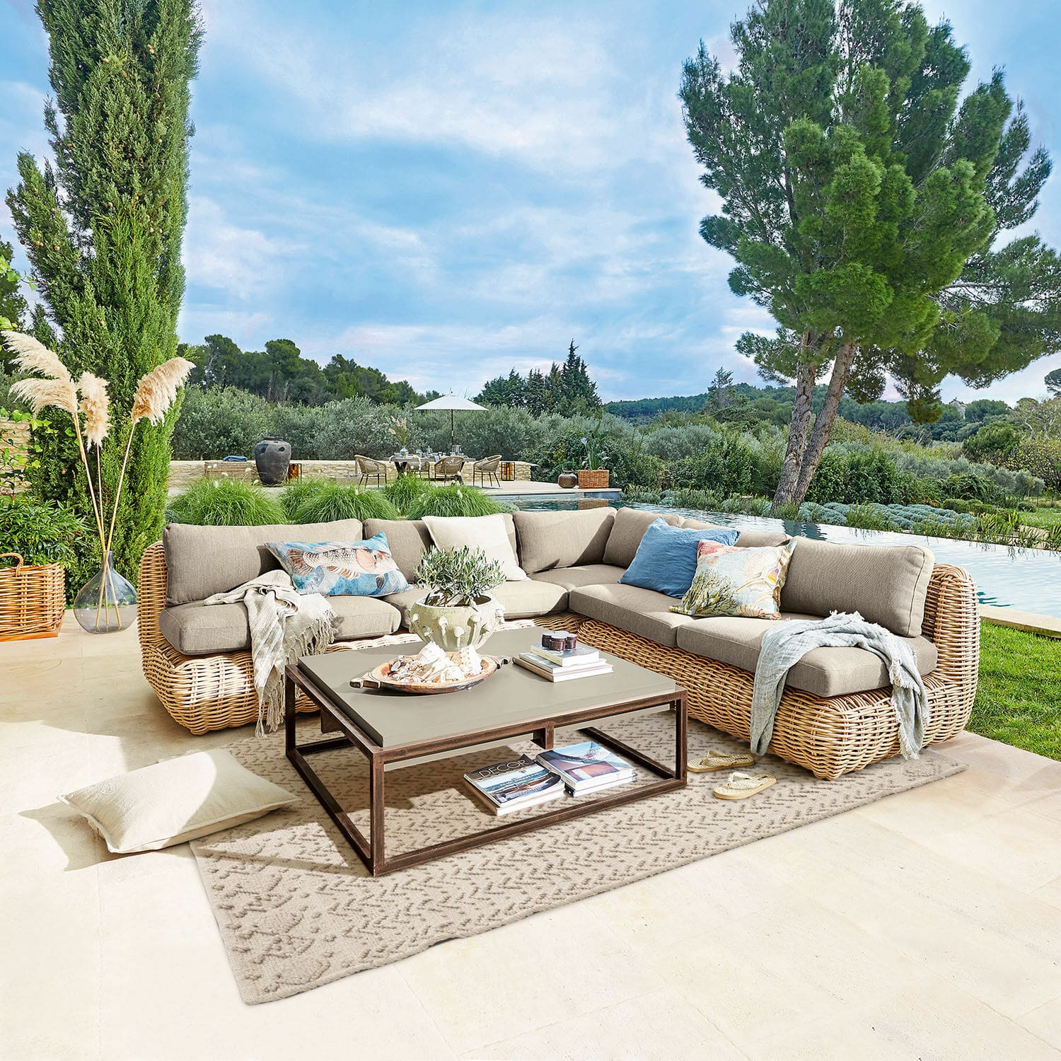 Buitenmeubelset met beige kussens en rotan frame op terras met uitzicht op zwembad