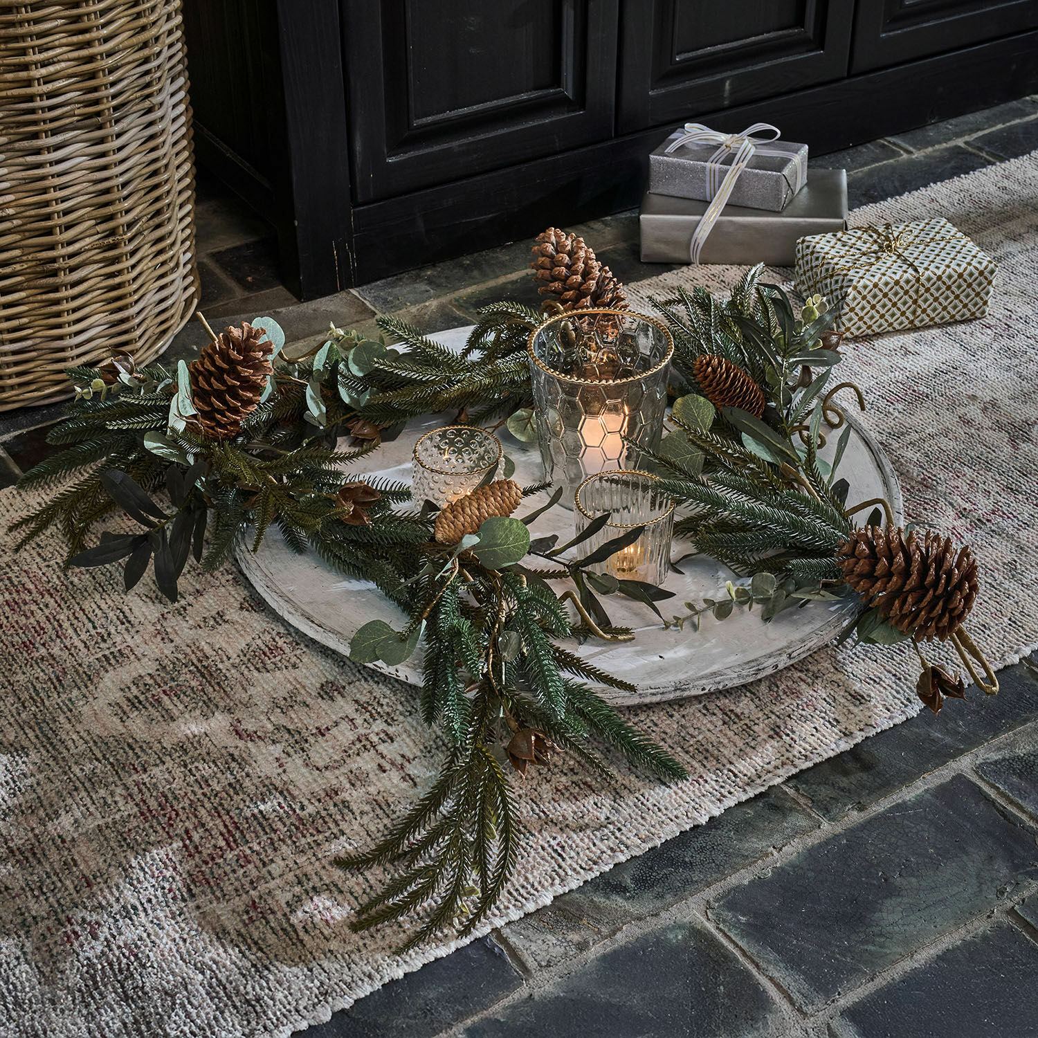 Guirlande Rosella Couronne décorative avec pommes de pin et branches vertes sur plateau clair avec lanternes et cadeaux