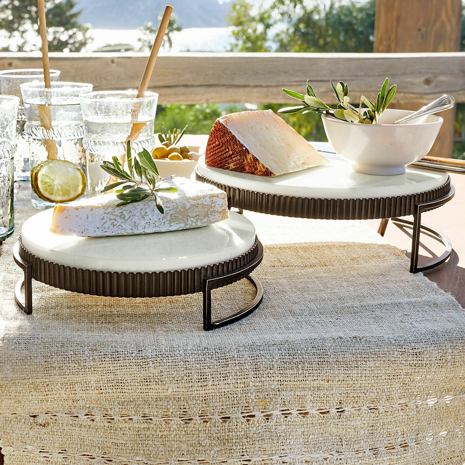 Lot de 2 plateaux Méridienn Deux plateaux ronds en marbre blanc avec support en métal, présentés avec fromages sur une table extérieure