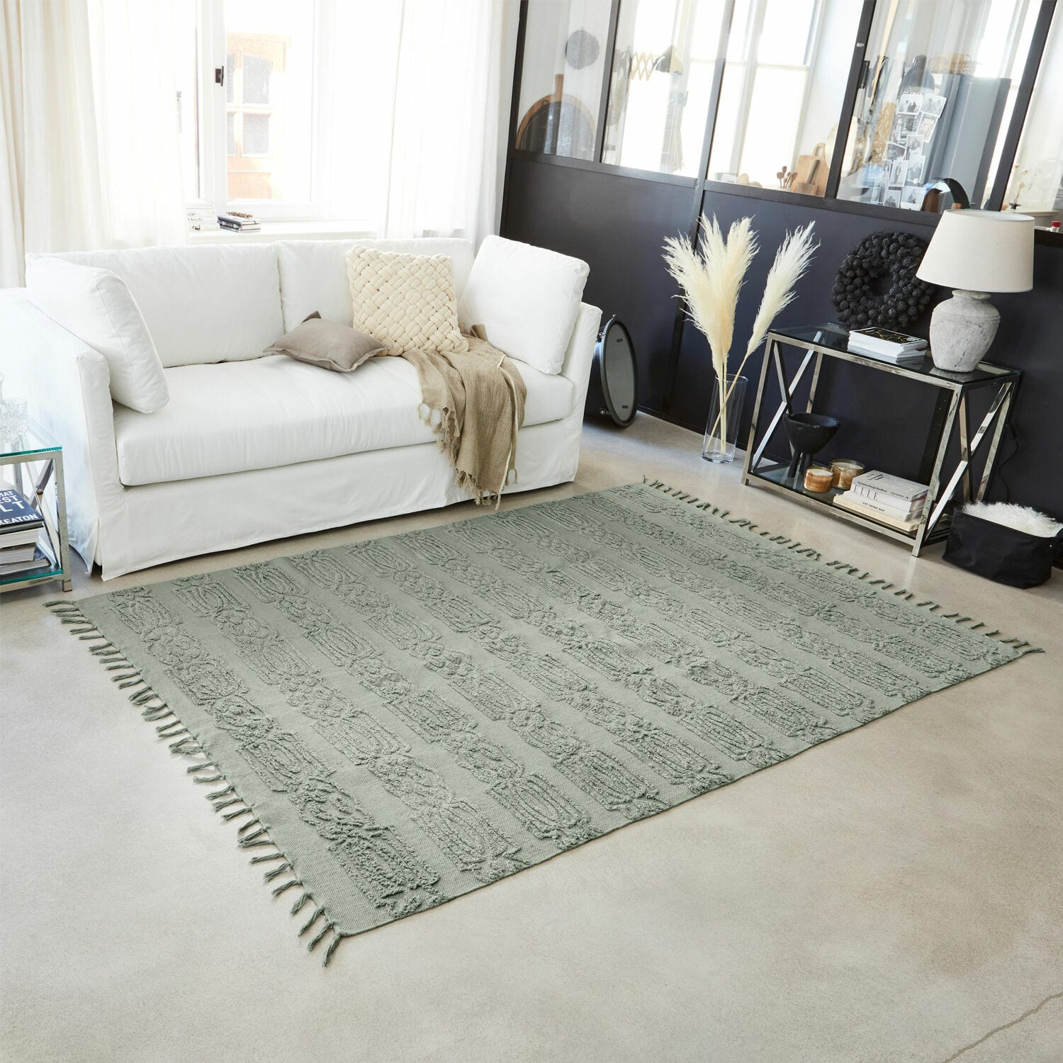 Tapis gris en coton avec motif décoratif et franges dans un salon moderne avec canapé blanc