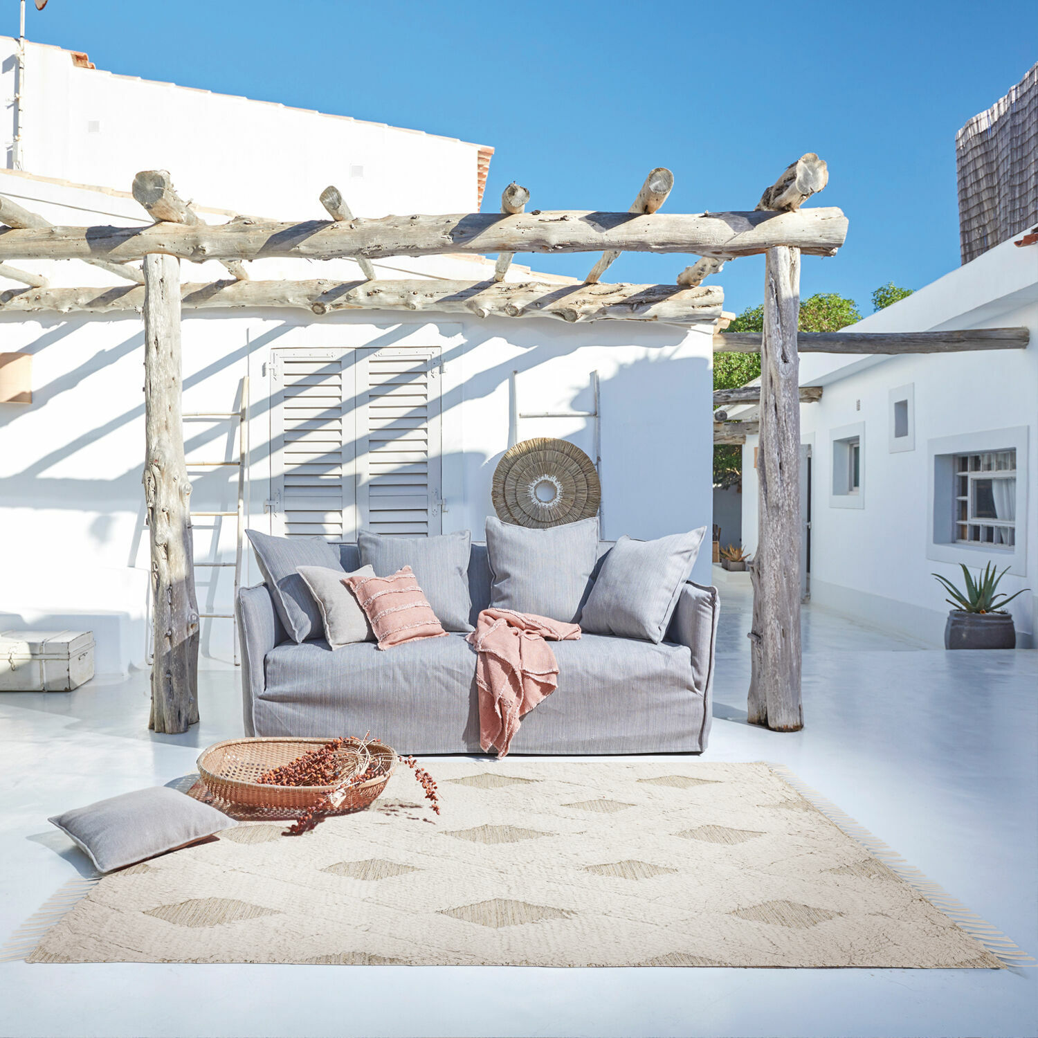 Tapis d’intérieur et d’extérieur Meagan Canapé gris en tissu sur terrasse avec tapis naturel et coussins roses pour détente extérieure