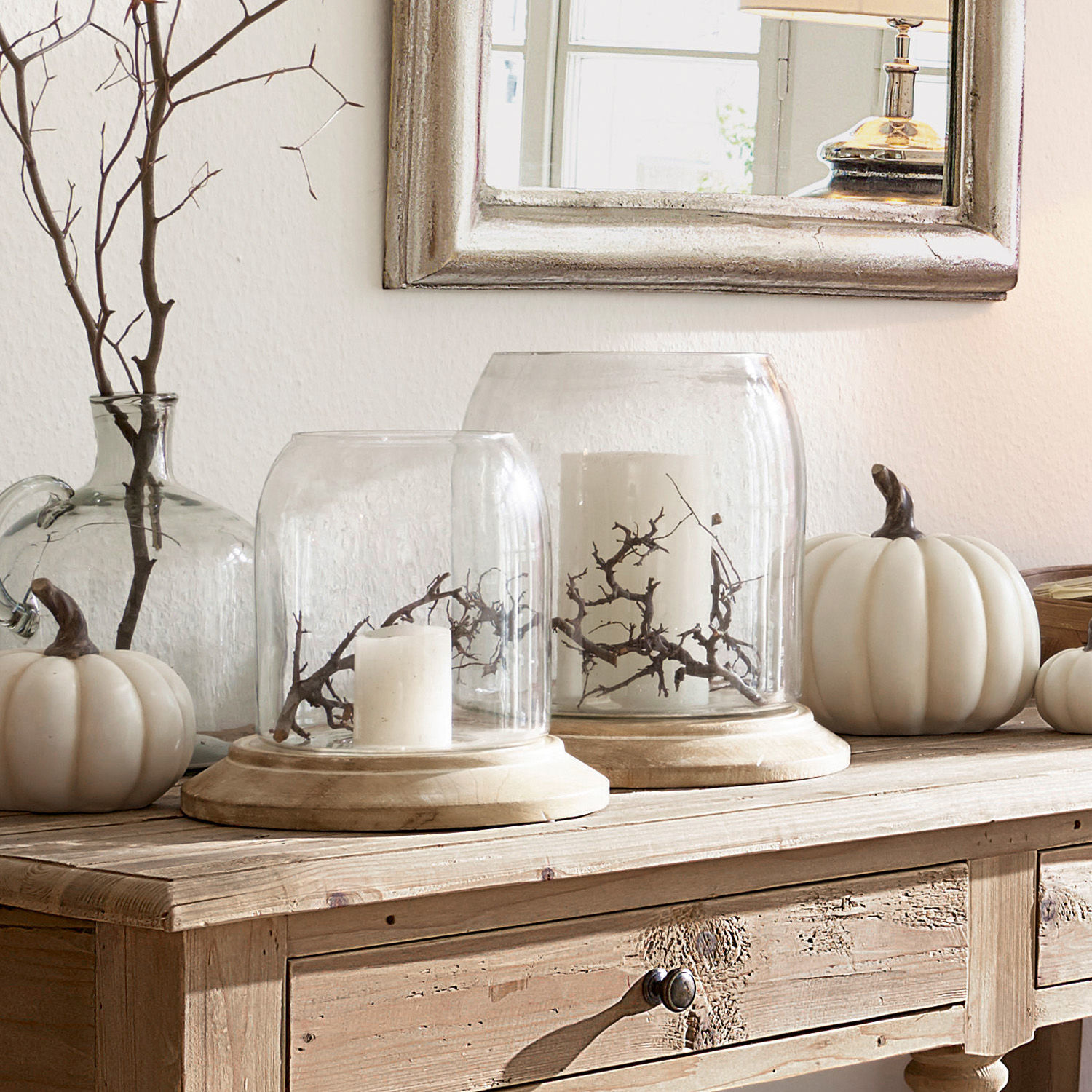 Cloche en verre décorative sur socle en bois avec bougies blanches et branches sur une table en bois