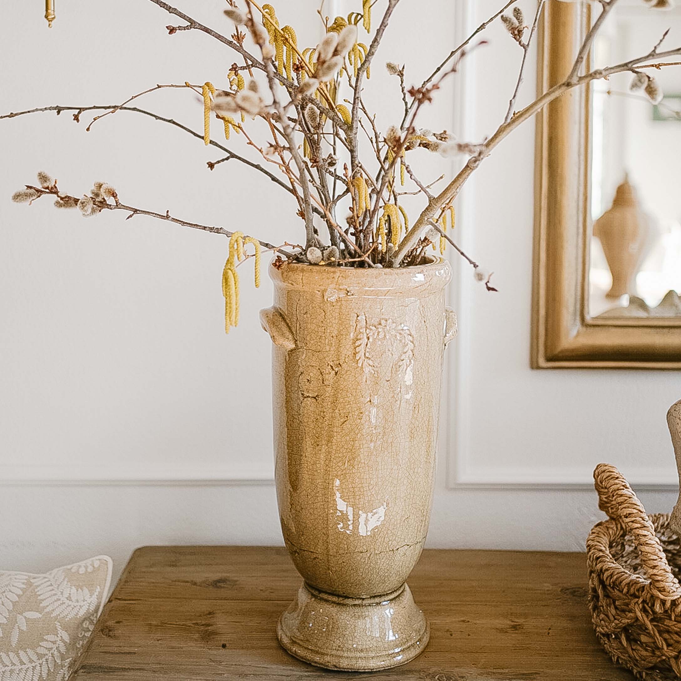 Vase en céramique beige avec branches et fleurs jaunes sur une table en bois dans un intérieur clair
