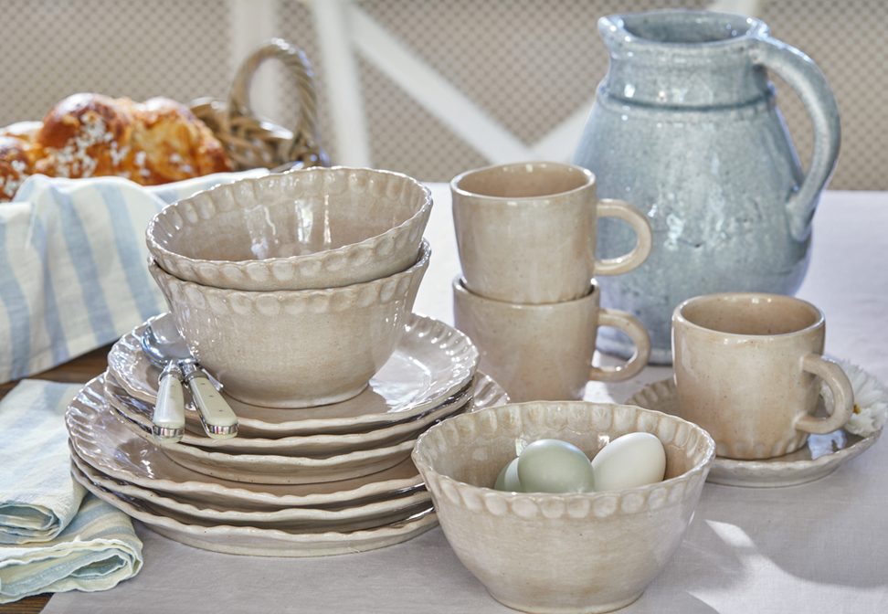 Service de vaisselle en céramique beige avec assiettes, bols et tasses sur une table rustique