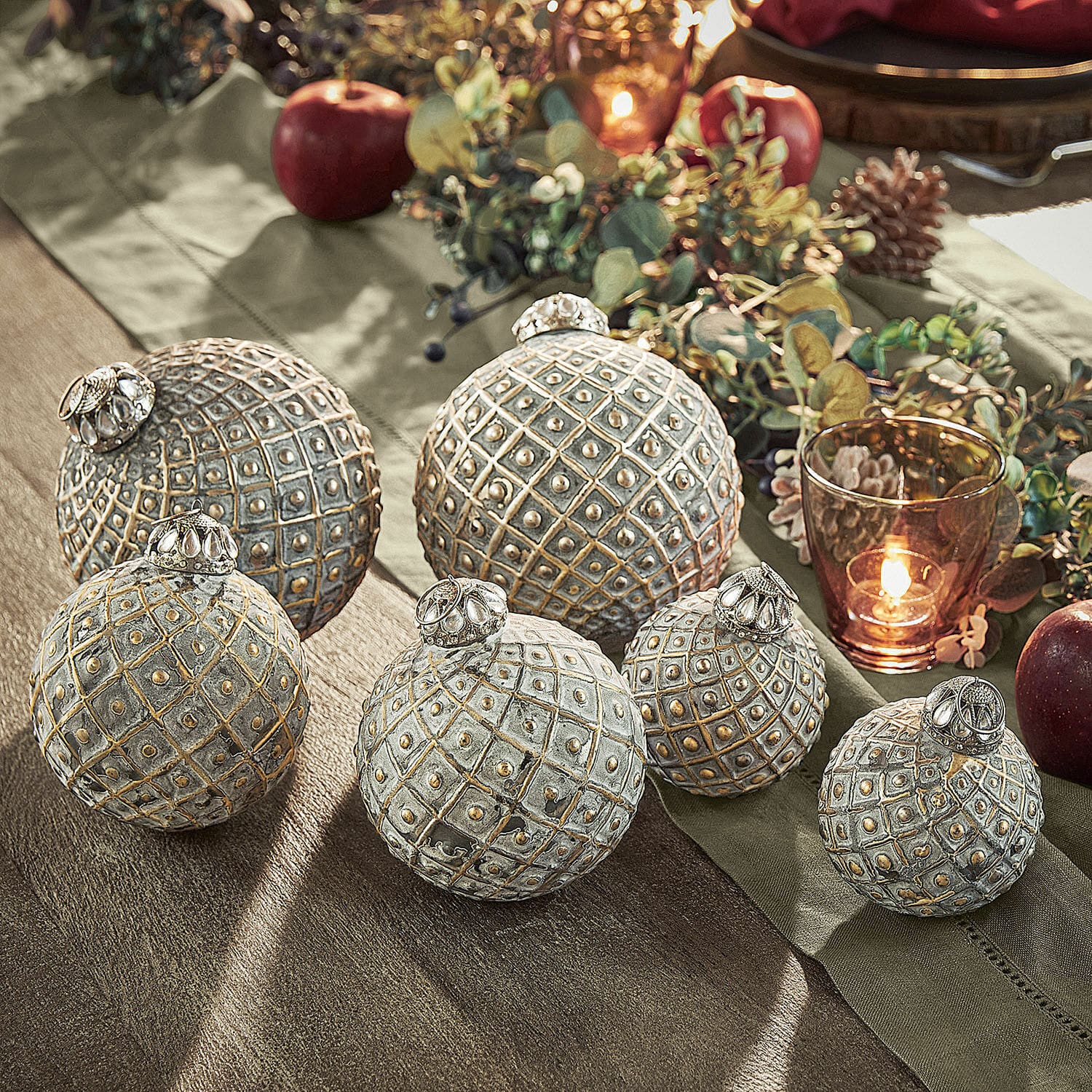 Lot de 6 décorations de Noël Lucero Ensemble de six boules décoratives en métal gris doré sur une table festive avec pommes et bougie allumée