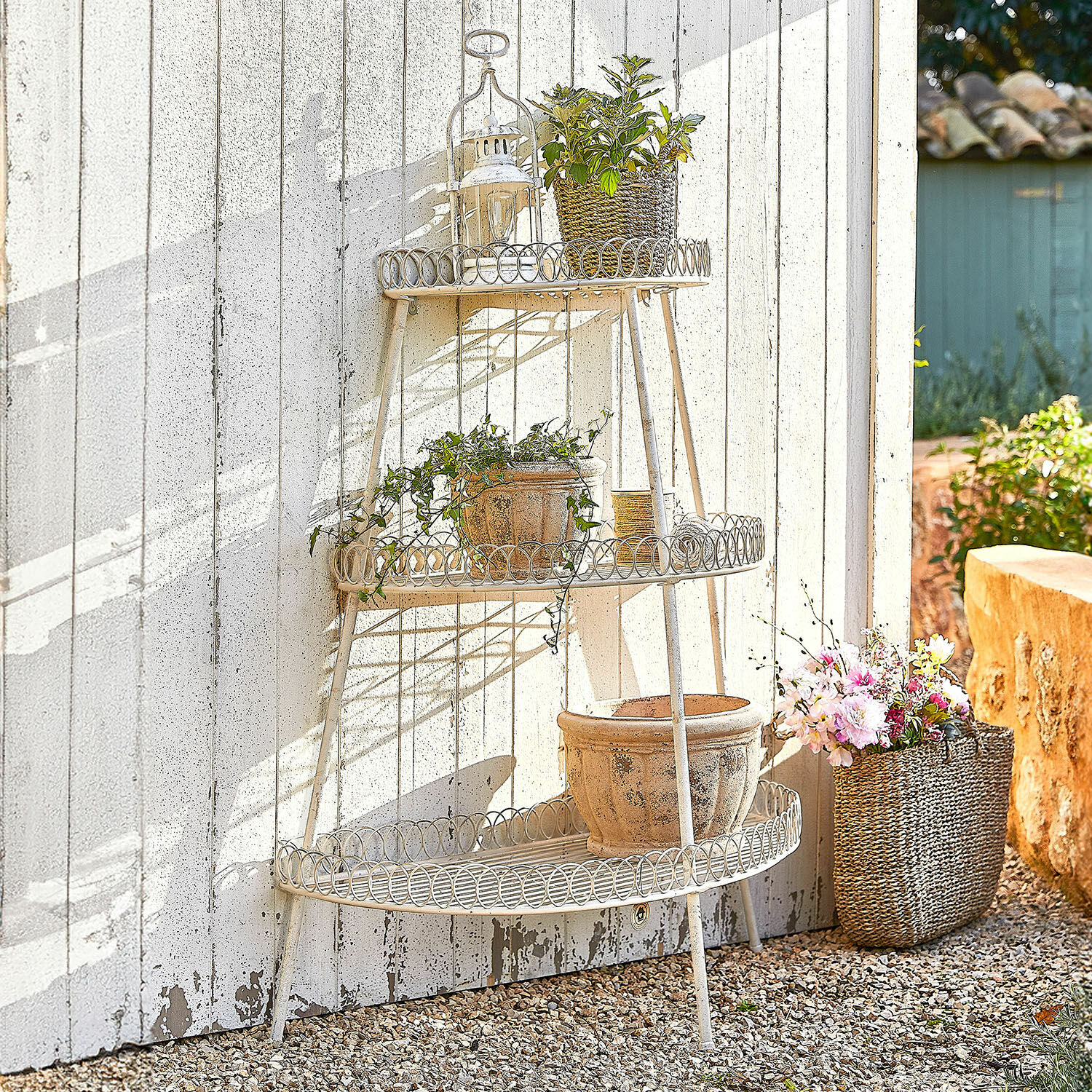 Etagère Lorivane Drie niveaus crème metalen tuinrek met bloempotten en planten tegen een witte muur