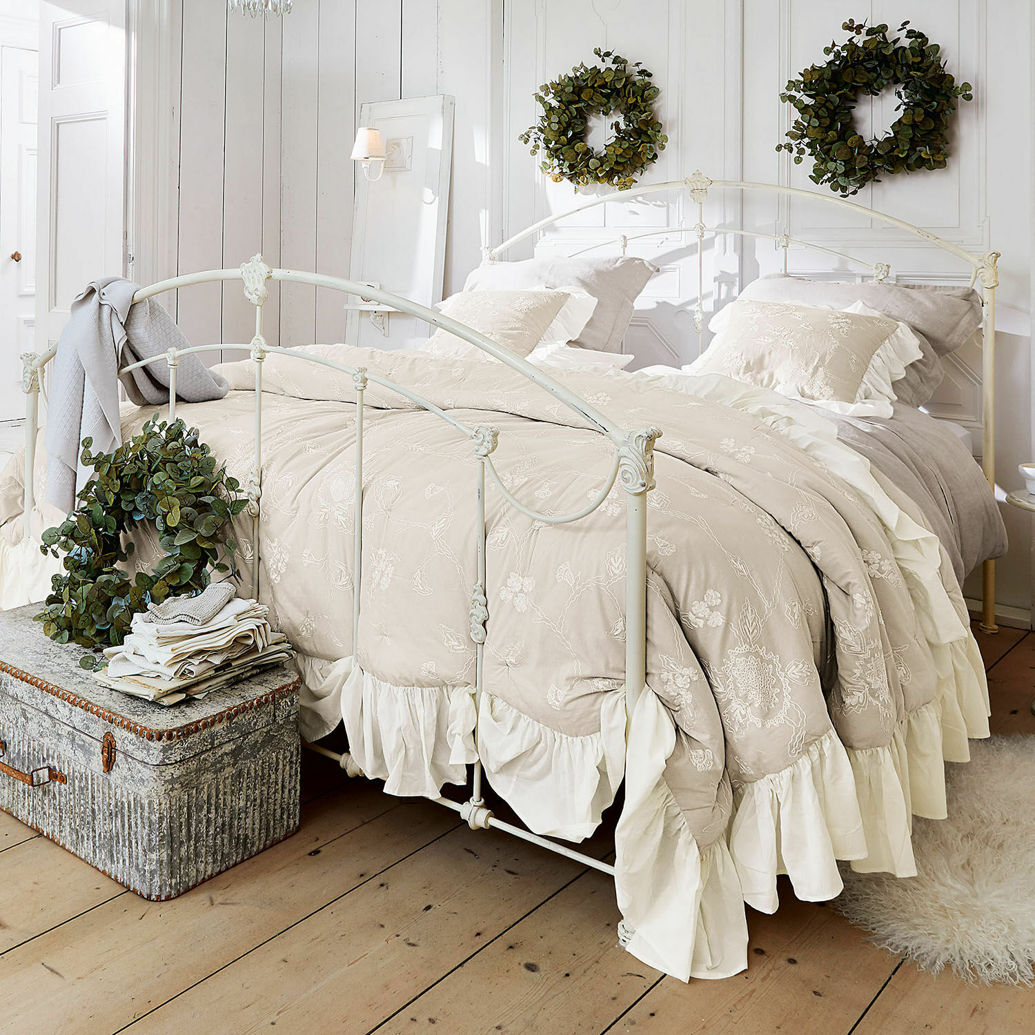 Quilt Clarissa Beige geborduurd beddengoed met ruches op wit metalen bed in lichte slaapkamer met groene kransen