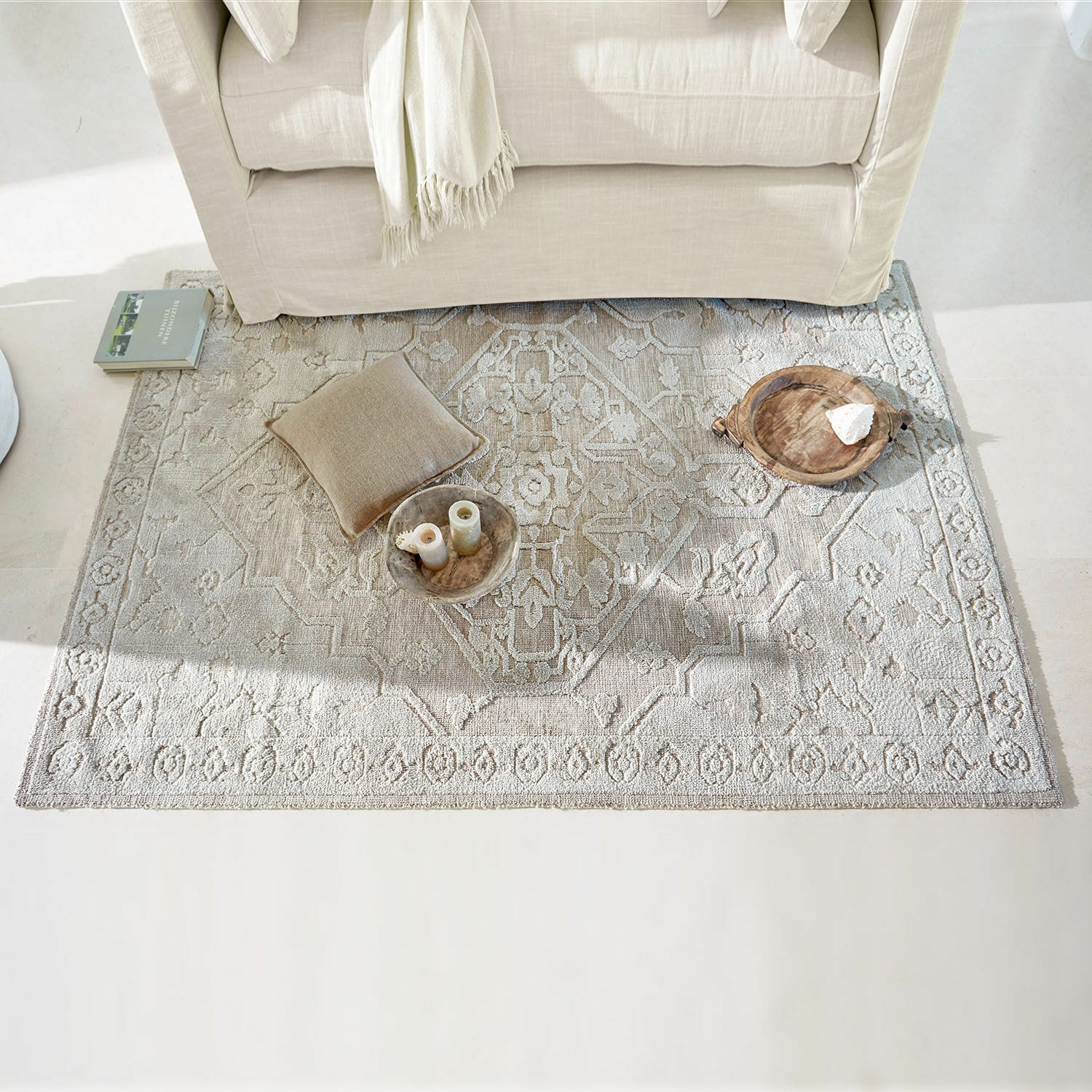 Tapis Armidale Tapis beige à motif sous un canapé clair avec coussin et décorations en bois dans un salon lumineux